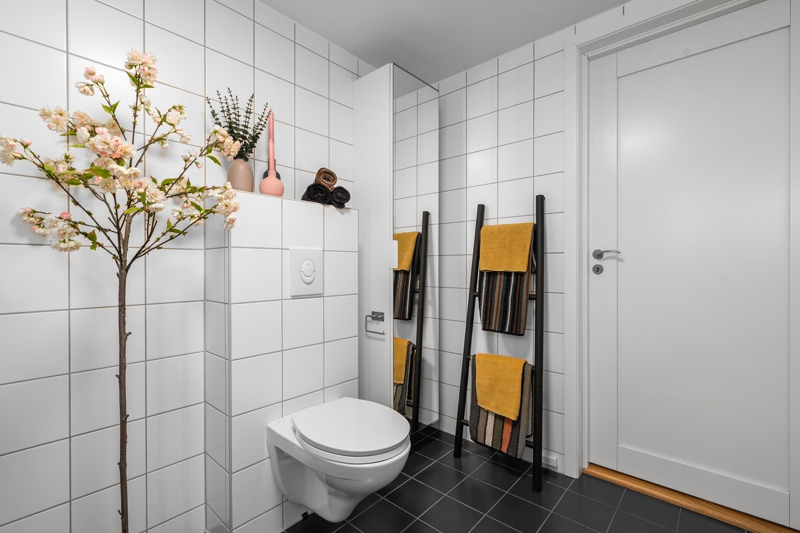 Badet er innredet med vegghengt toalett, dusjhjørne med innfellbare glassdører og vegghengt servantskap med heldekkende servant Galleribilde
