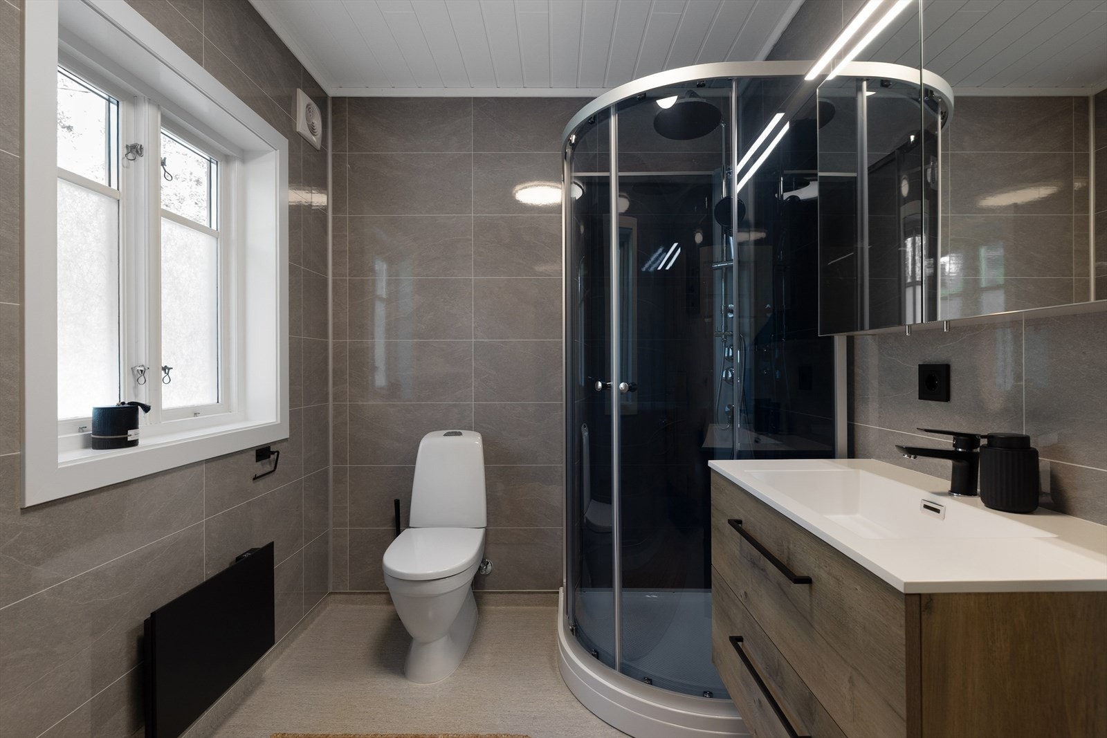 Det er nye baderomsplater på vegg, nytt toalett, ny innredning og nytt dusjkabinett med bunn. Galleribilde