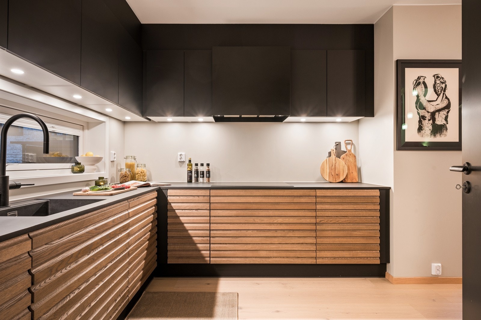 Stilrent kjøkken med spilede underskap, elegante sorte overkap og slitesterk laminatbenk med underlimt vask og matchende sort armatur Galleribilde