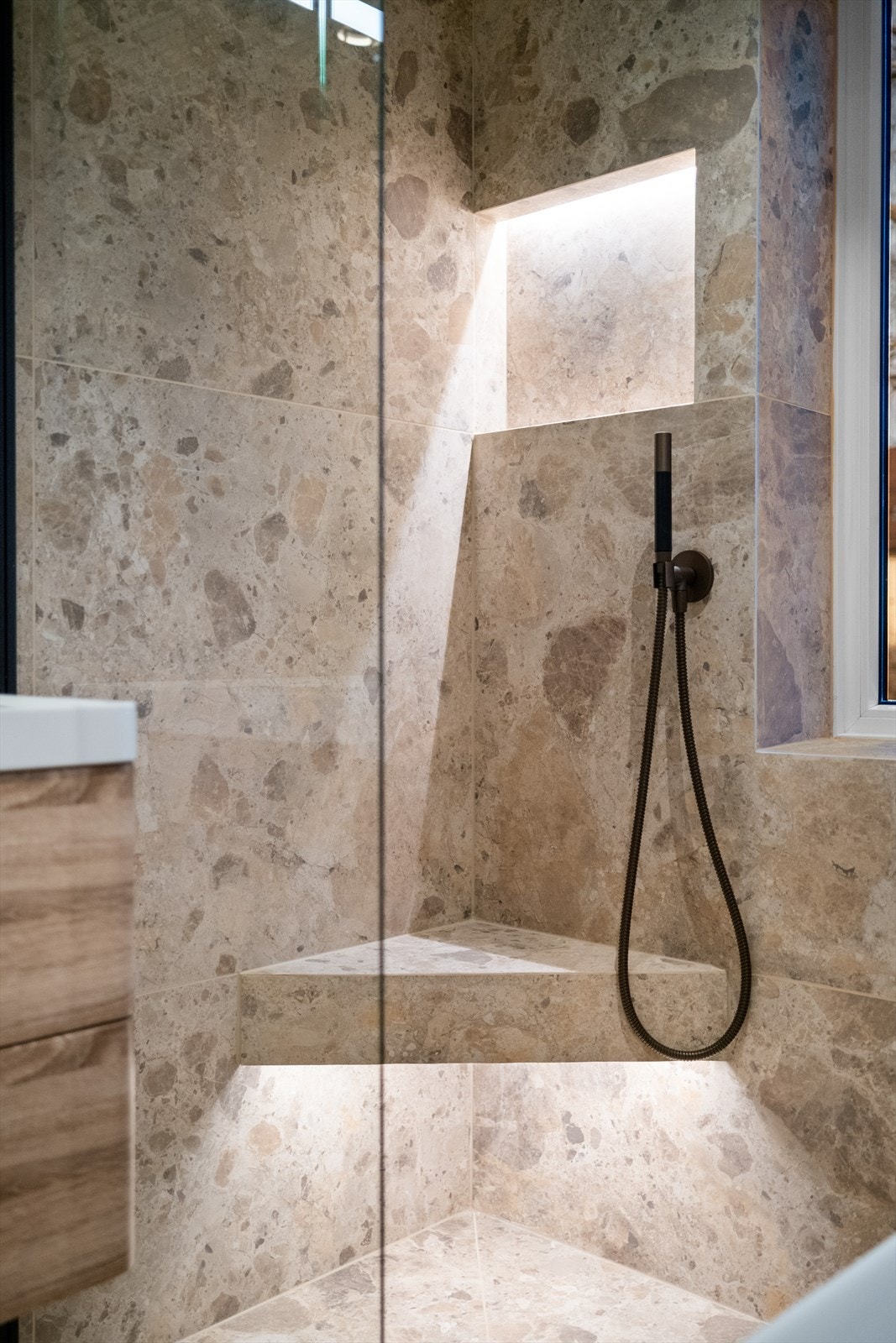 Dusjnisjé med benk og innfelt hylle med belysning. Baderommet er innredet med vegghengt klosett, servant med innredning, speil med lys, håndkletørker med varme, dusjhjørne med glassvegg og badekar. Galleribilde