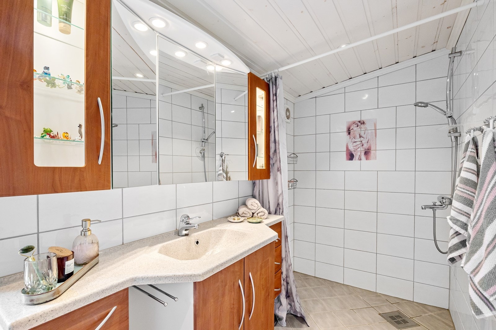 Badet er innredet med dusjhjørne, vegghengt toalett, servant med møblement og overskap med speil og belysning. Galleribilde