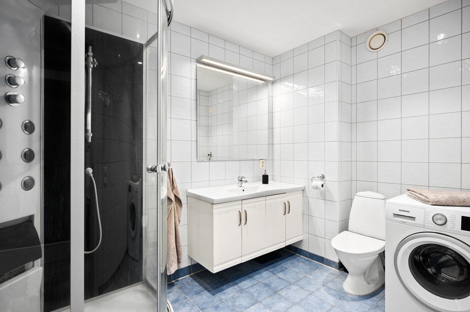 Helfliset bad med varmekabler i gulv. Rommet er innredet med dusjkabinett, gulvstående toalett og vegghengt servant Galleribilde