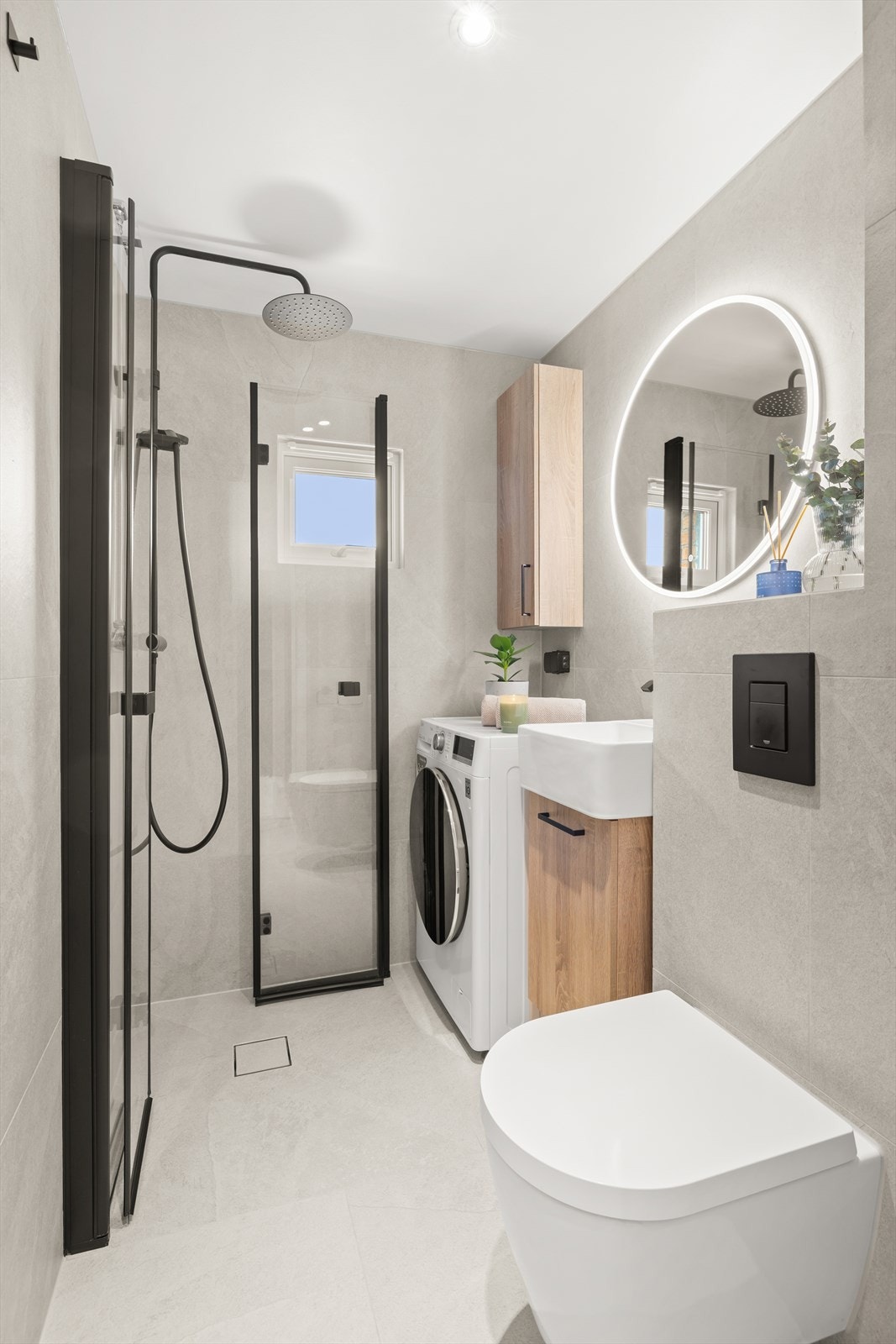 Delikat og strøkent baderom med praktisk dusjhjørne, servant med innredning, toalett og opplegg for vaskemaskin Galleribilde