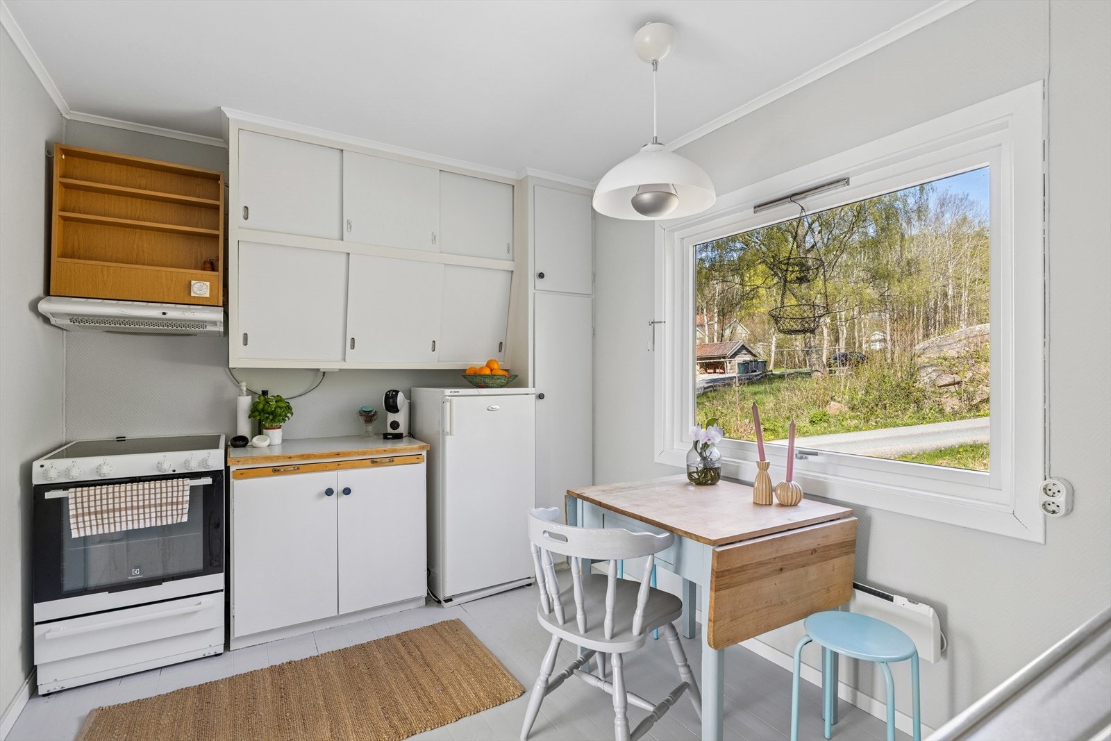 Kjøkkeninnredning med glatte fronter. Skråstilte overskap med skyvedører. Belysning under overskap. Fliser på vegg over benkeskap. Laminat benkeplate. Galleribilde