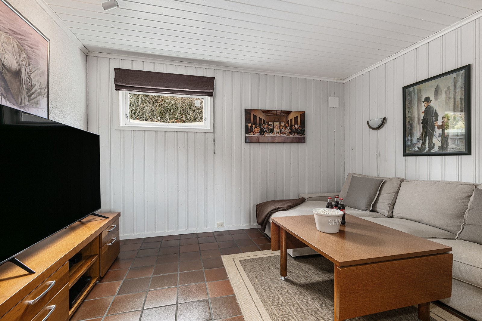 Kjellerstuen har åpen tilknytning til en tv-stue med sofa og tv-benk Galleribilde