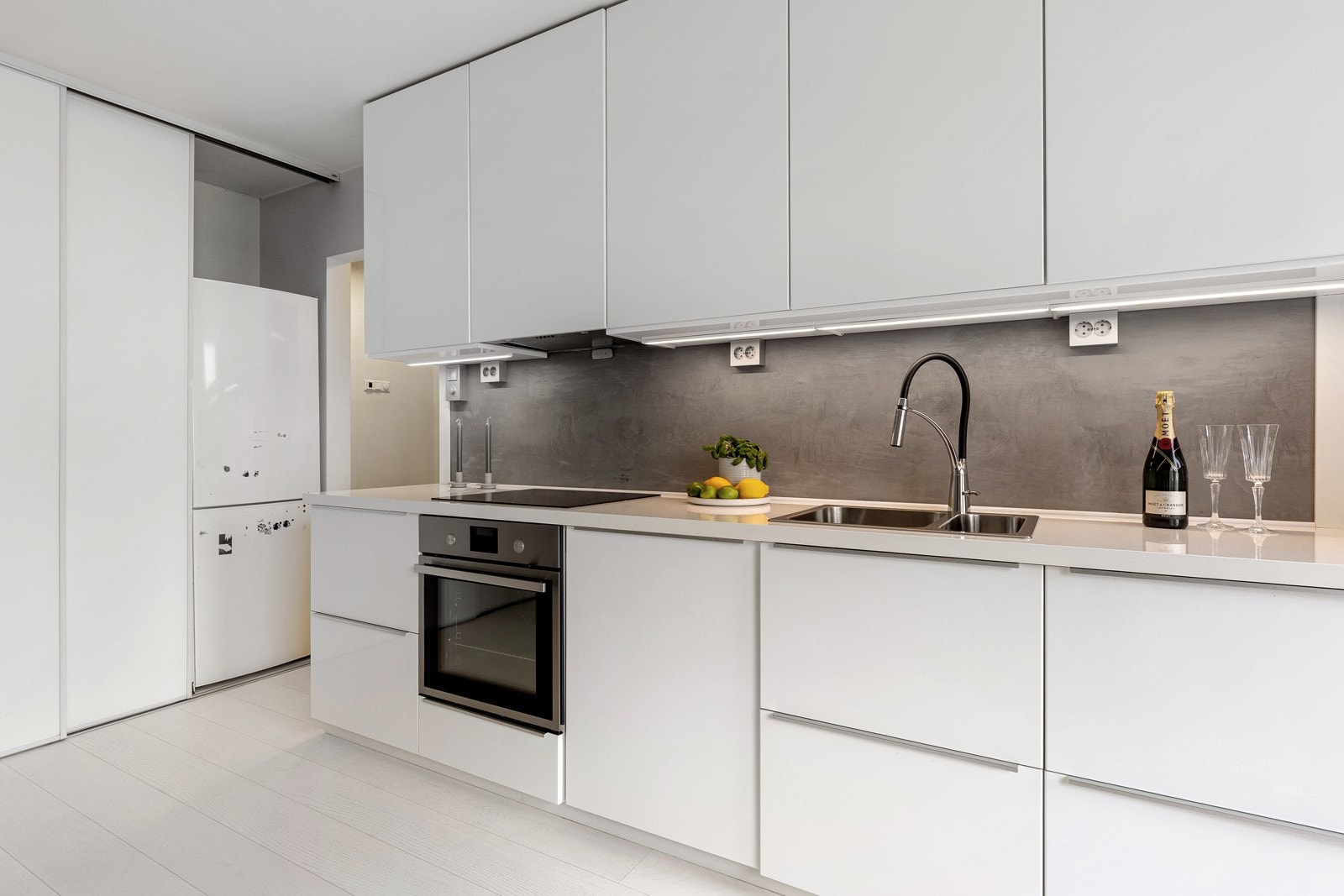 Kjøkkenet er innredet med slette fronter i hvit høyglans og laminerte benkeplater med nedfelt oppvaskkum. Galleribilde