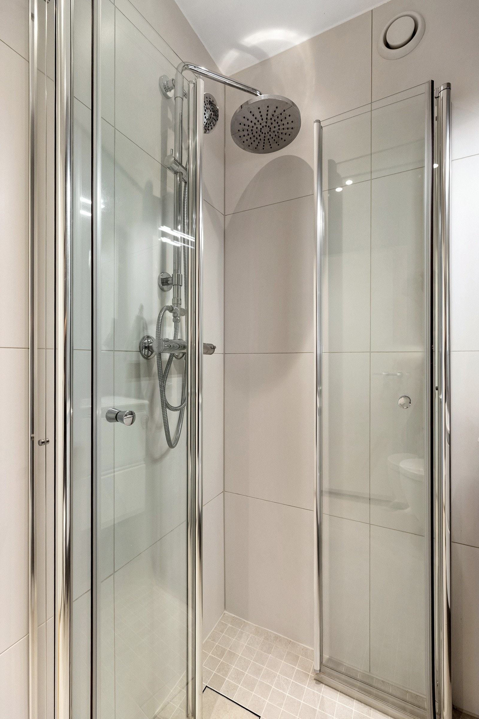 Rommet er utstyrt med et dusjhjørne med svingbare foldedører i glass, vegghengt toalett, moderne servantinnredning og et overskap med speildører over servanten. Galleribilde