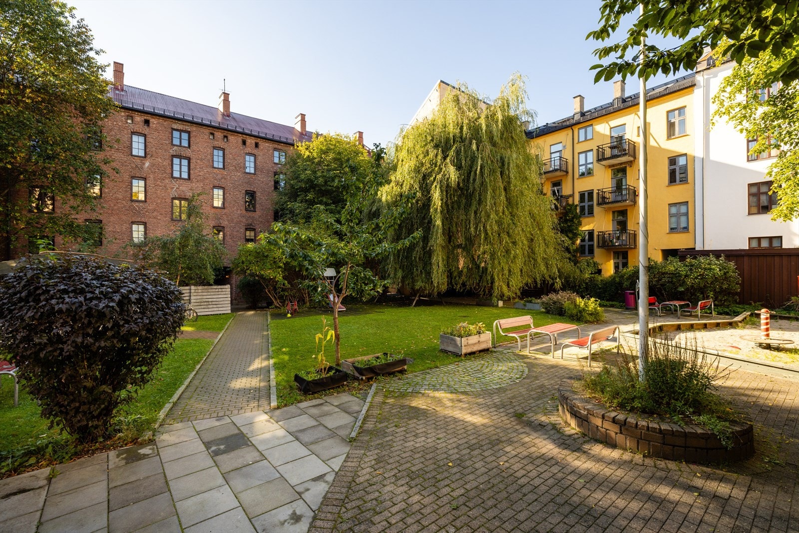 Idet du kommer innenfor porten i dette borettslaget kommer du inn i en skjermet og idyllisk oase med bugnende beplantning, trær, mange hyggelige sittegrupper til stor glede for beboerne. Galleribilde