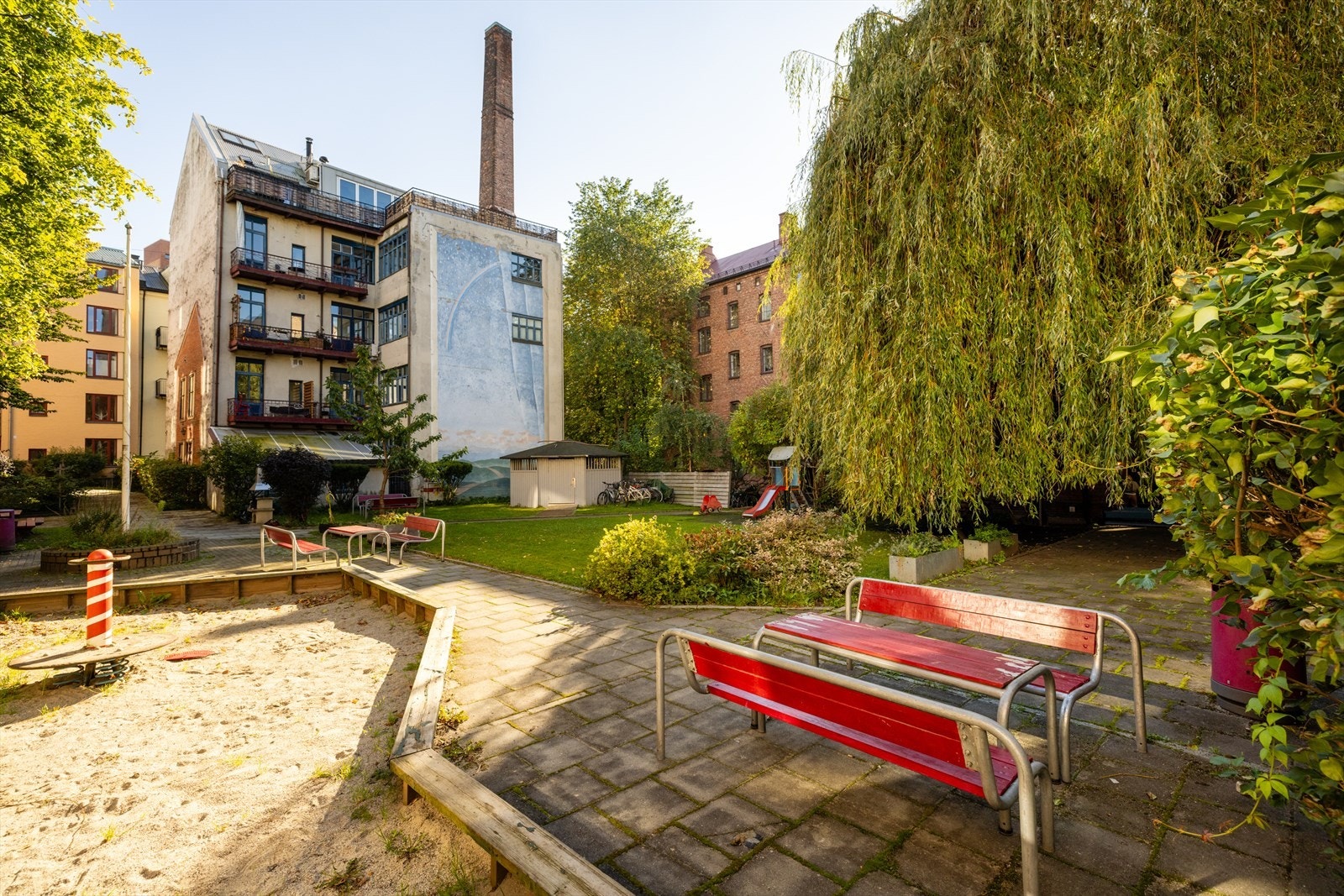 Skjermet og pent opparbeidet bakgård hvor både store og små trives! Her finner du hyggelig beplantning, koselige sittegrupper, mange trær, stensatte gangveier og lekeplasser for de små. Videre finner du plenarealer og vakre prydbusker! Galleribilde