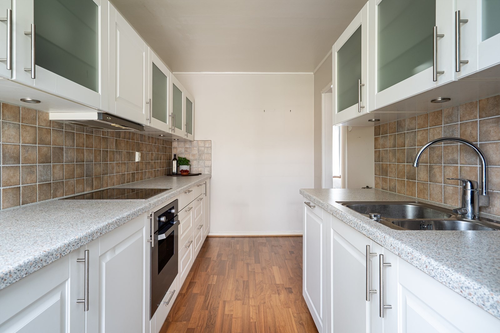 Innredningen er holdt i en klassisk stil med hvite, profilerte fronter, frostede vitrineskap og benkeplate i grå laminat med vaskekum i stål. Galleribilde