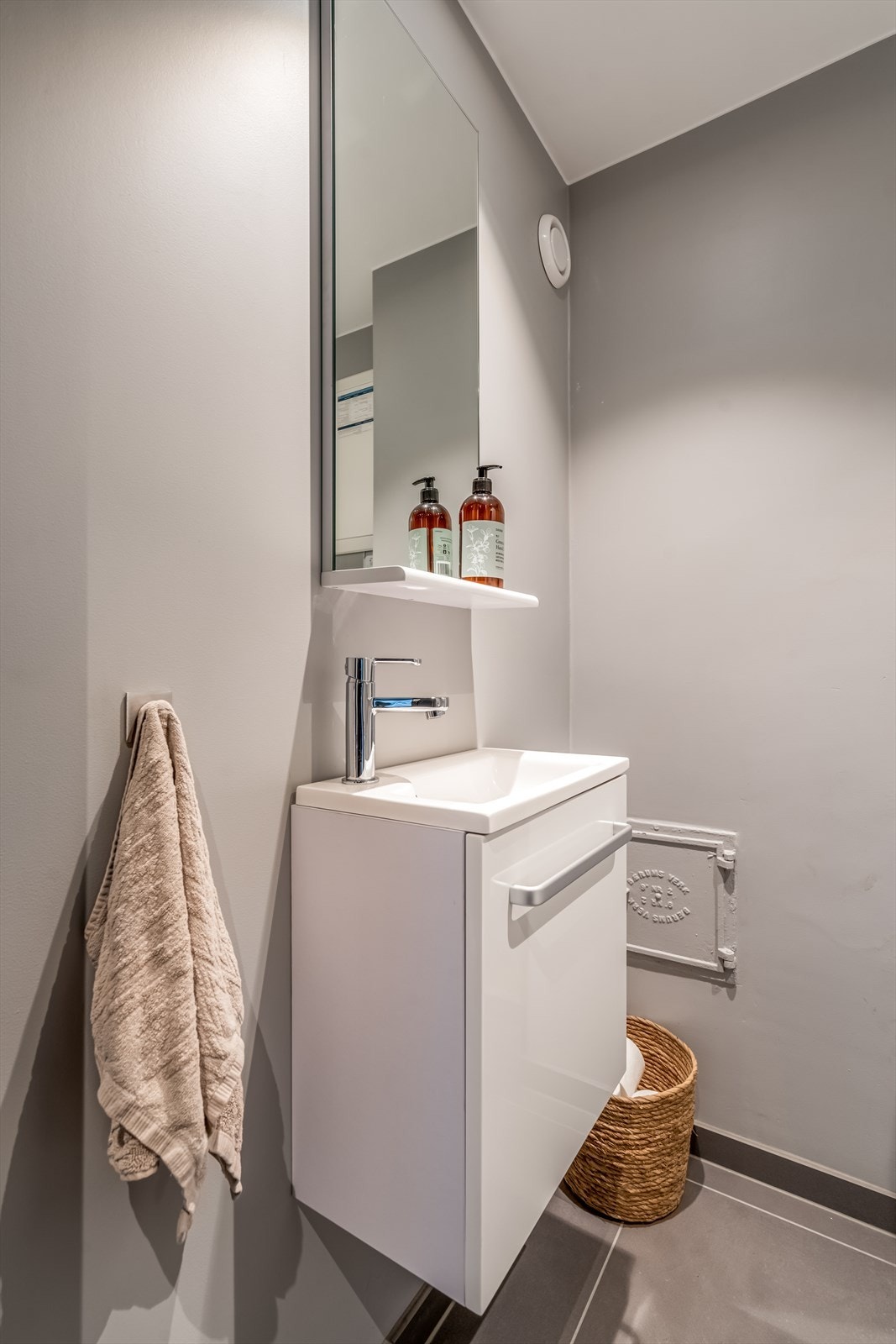 WC med 60*60 fliser, vegghengt toalett, liten servant med underskap og speil samt spott i tak. Galleribilde