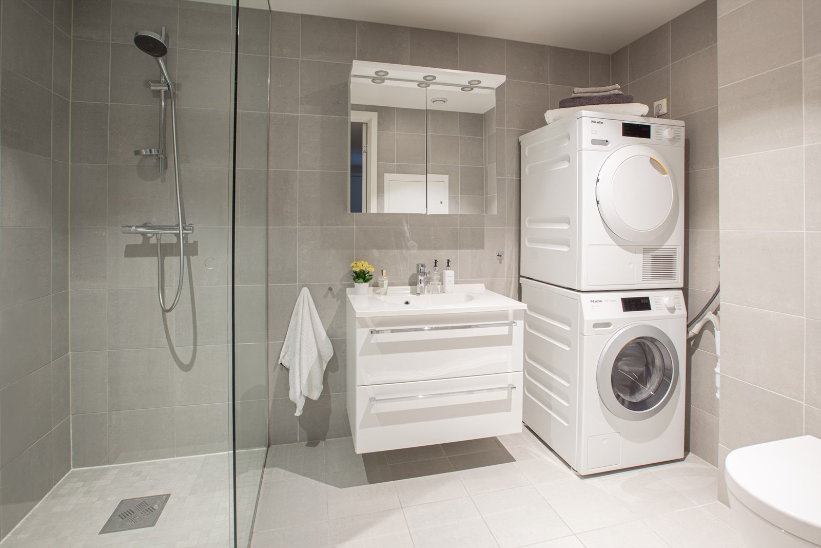 Badet har vegghengt servant med overspeil, vegghengt toalett, samt et dusjhjørne med en glassdør som strekker seg til taket. Galleribilde