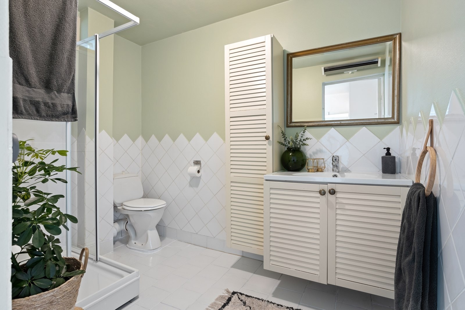 Eldre bad med keramiske fliser på vegg opp til ca. 1,21 meter. Derfra er det platede vegger belagt med strie og keramiske fliser på gulv. Galleribilde