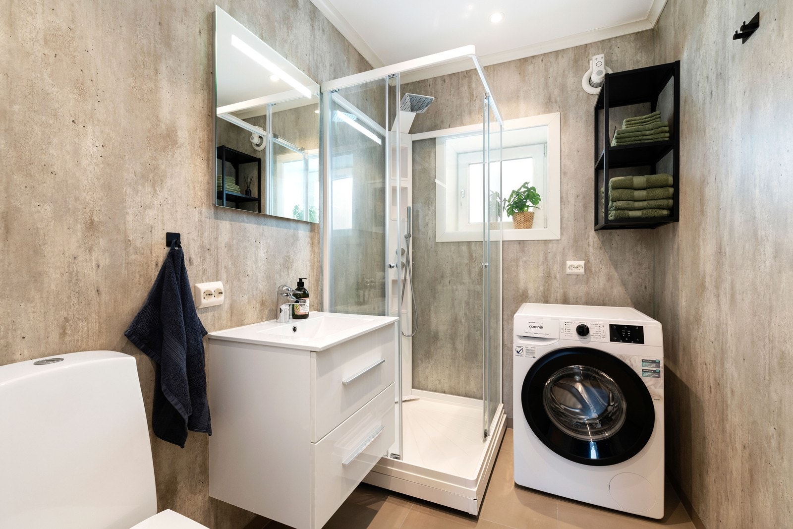 Moderne bad med fliser på gulv og våtromsplater på vegger. . Badet har dusjkabinett, servant med underskuffer, toalett og opplegg til vaskemaskin. Galleribilde