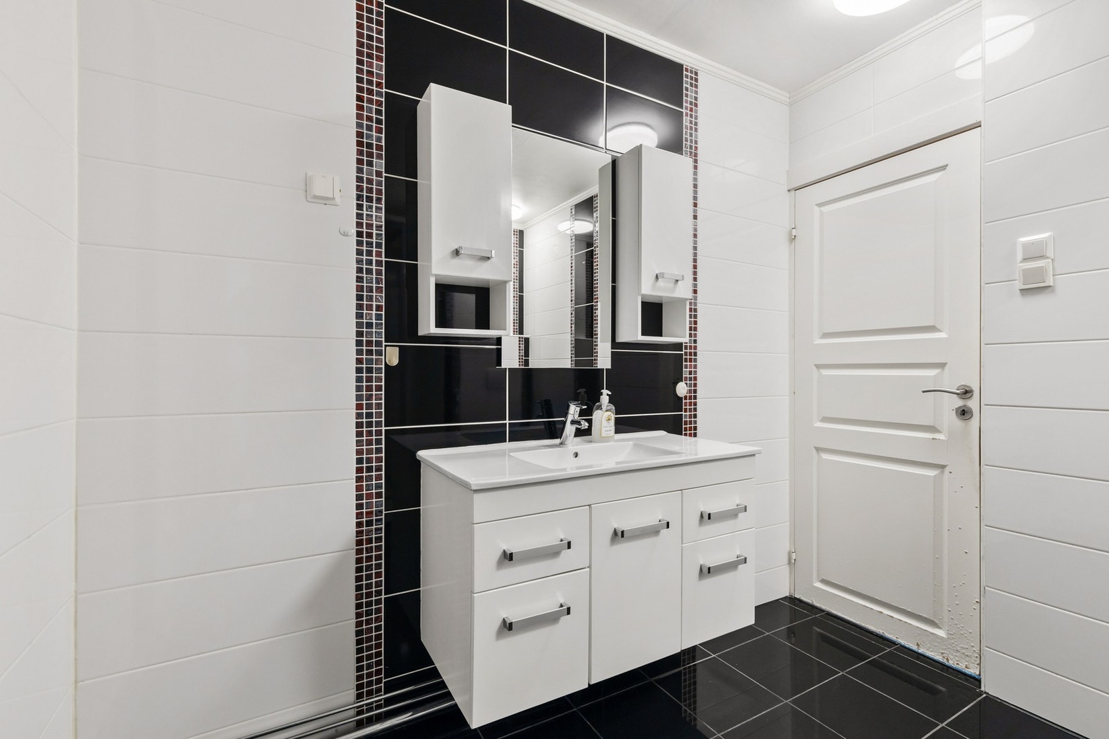 Det er montert en vegghengt servantinnredning med skuffer og dør, samt en ovenpåliggende servant med ett-greps armatur. Over servanten er det speil og vegghengte skap Galleribilde