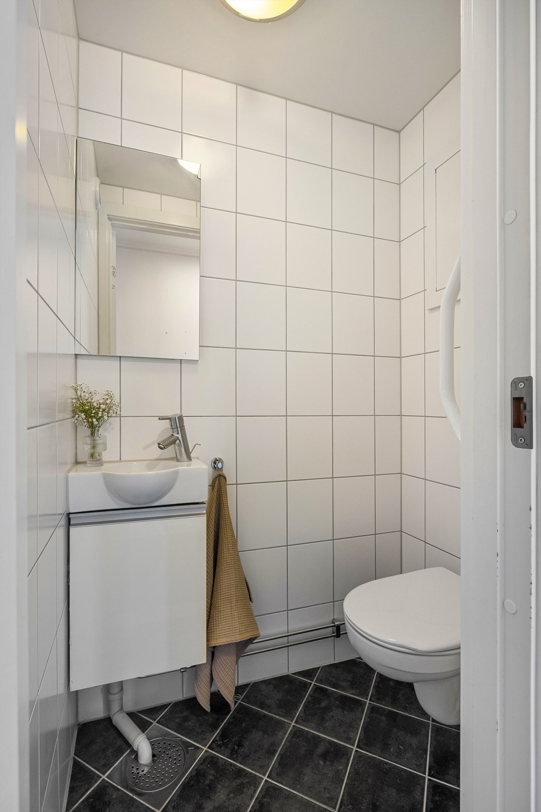 Badet inneholder dusjhjørne med innfellbare dører i glass og baderomsinnredning med servantskap, heldekkende servant med ett-greps blandebatteri og speil med lysarmatur på vegg. Galleribilde