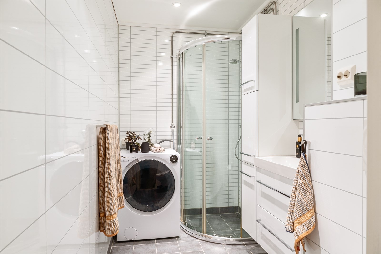 Badet har våtromsplater på vegger og fliser på gulv. Det er varmekabler i gulv på badet. Badet er innredet med dusjhjørne, vegghengt toalett, vask i seksjon og opplegg for vaskemaskin. Galleribilde