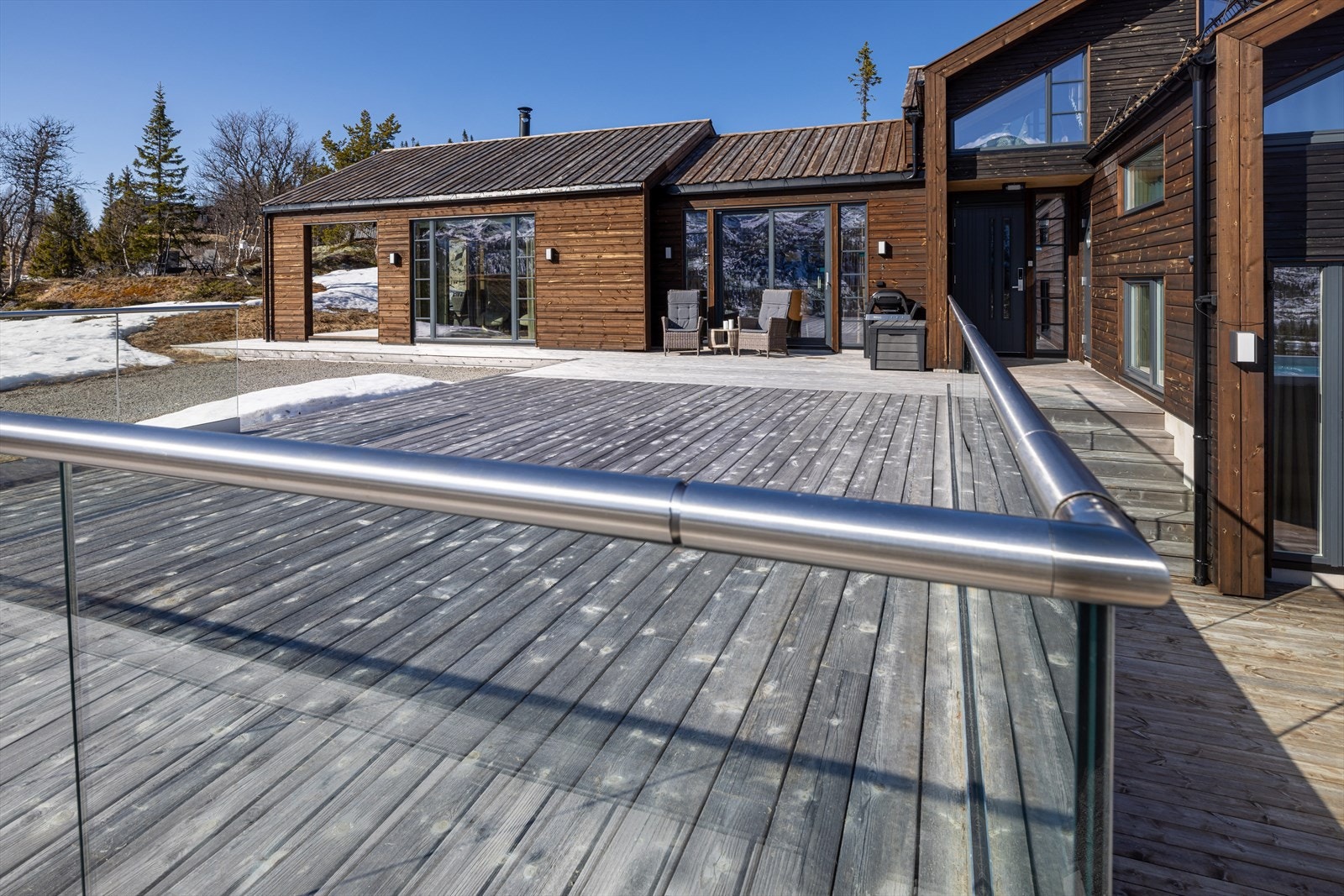 Stor terrasseflate med rekkverk i glass og stål som gir et moderne uttrykk og fri utsikt mot omgivelsene Galleribilde