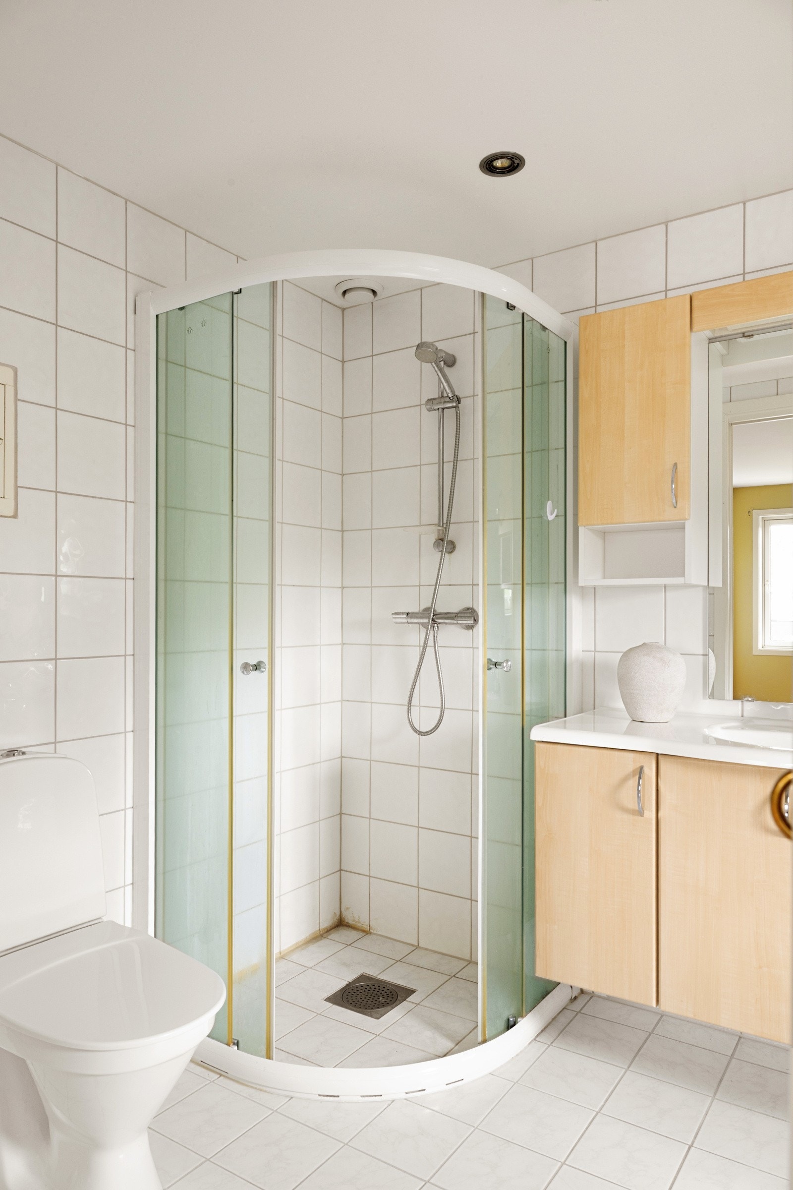 Badet har hvite fliser på veggene og lyse fliser på gulv med gulvvarme, og det er god oppbevaringsplass i en stilren innredning med heldekkende servant Galleribilde