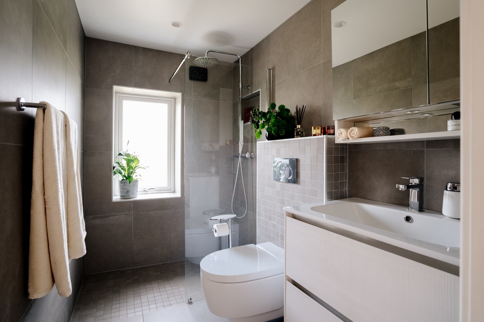 Badet er utstyrt med et vegghengt Geberit-toalett med elektrisk spylefunksjon, og et dusjhjørne med glassvegg og regndusj. Galleribilde