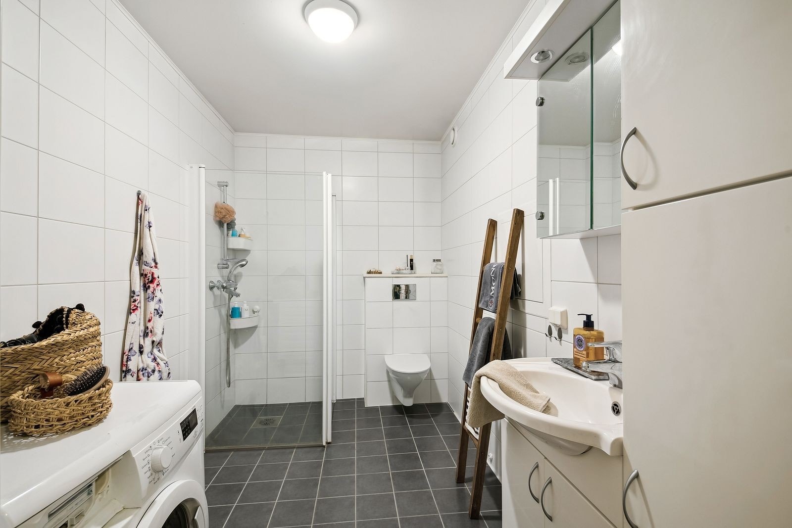 Pent flislagt bad med vaskemaskin og innfellbare dusjdører, godt med oppbevaringsplass i skap Galleribilde