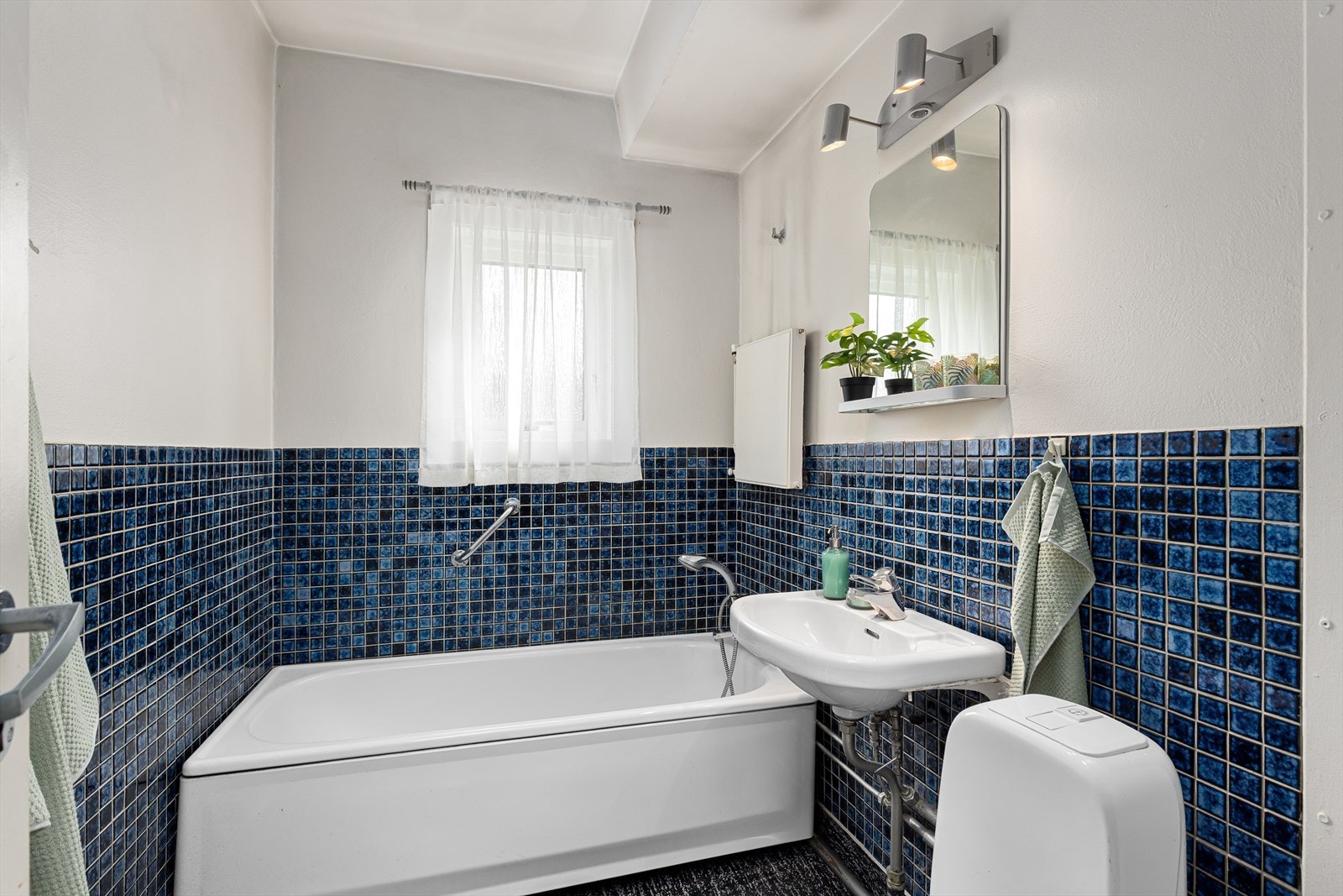 Eldre, men koselig baderom med badekar, gulvstående klosett og servent med speil og belysning Galleribilde