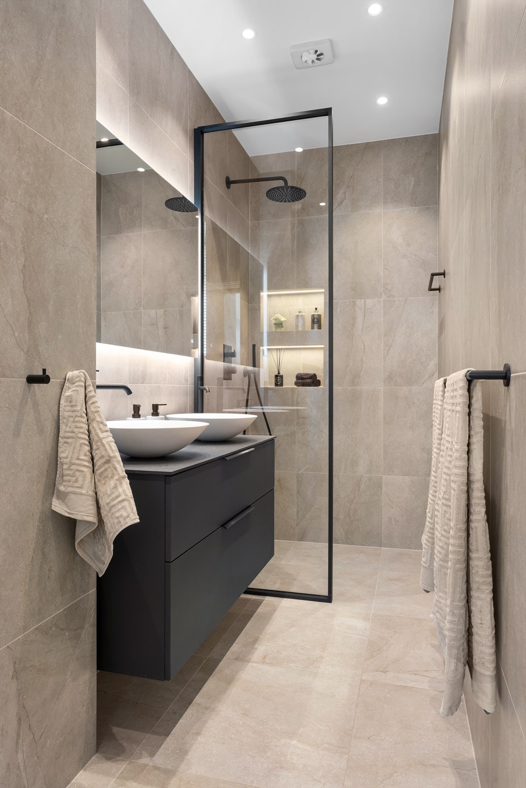 Baderomsinnredning med dobbel servant, Tapwell-kraner og store skuffer. Spesialtilpasset glassvegg og integrert dusjarmatur fra Tapwell med takdusj og hånddusj. Det er også hyller med integrert belysning i dusjsonen. Fuktstyrt vifte i taket. Galleribilde