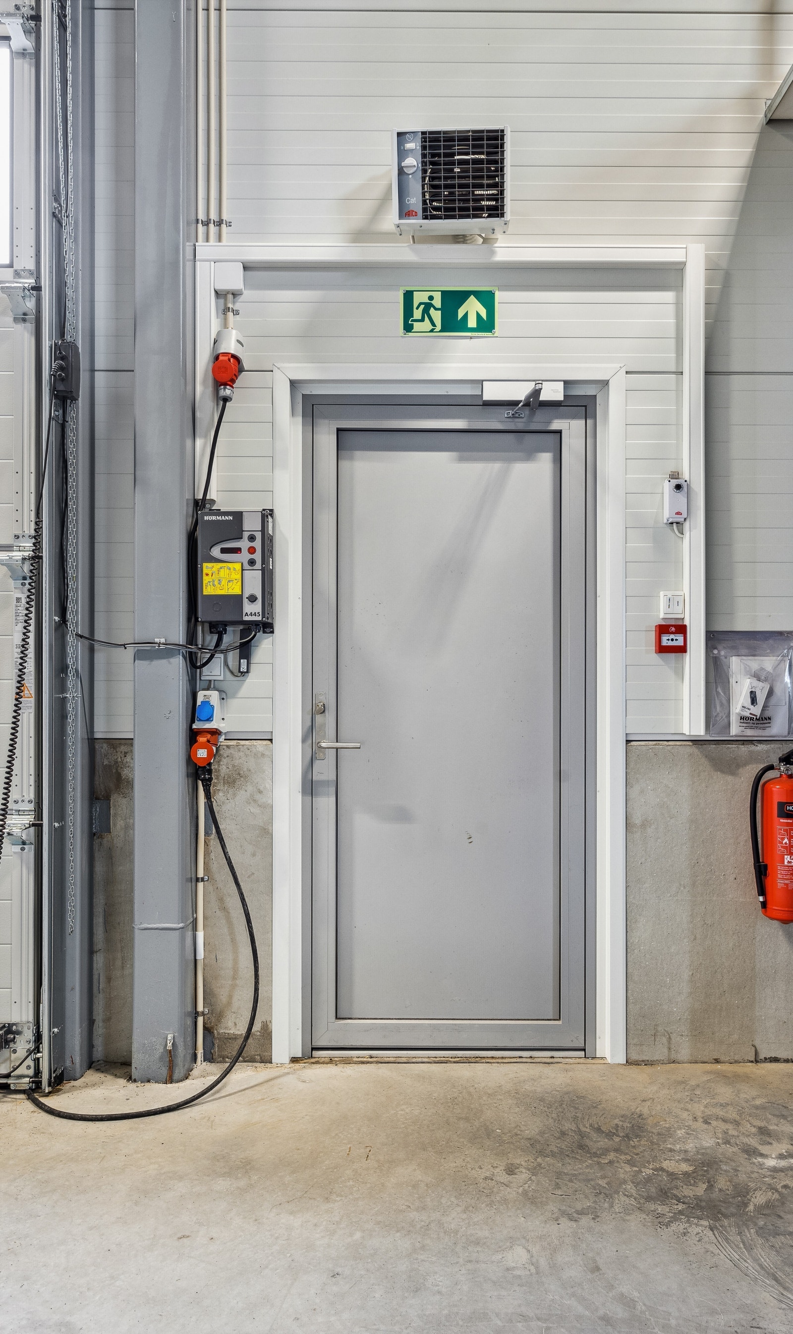 Varmeovn over dør, med brannslukkingsapparat og bryter/kontrollpanel til elektrisk leddheisport. Galleribilde