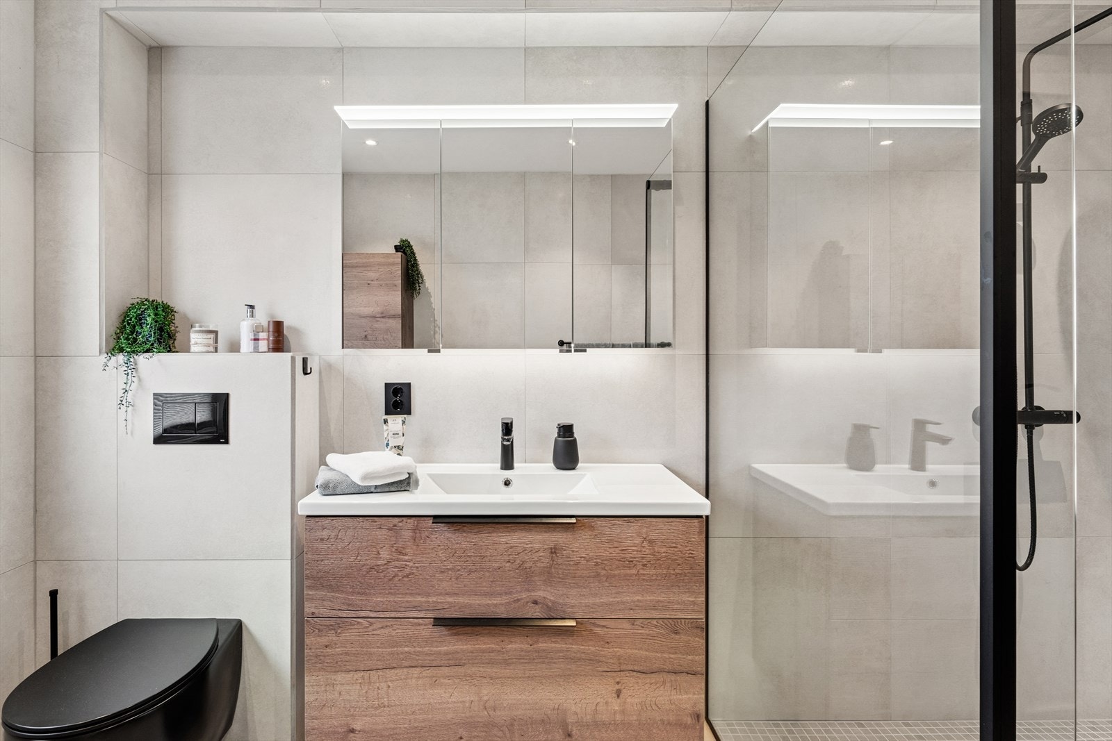 Videre er det et romslig dusjhjørne med glassdører, en moderne servantinnredning, speilskap med lys, vegghengt toalett og et høyskap. Galleribilde