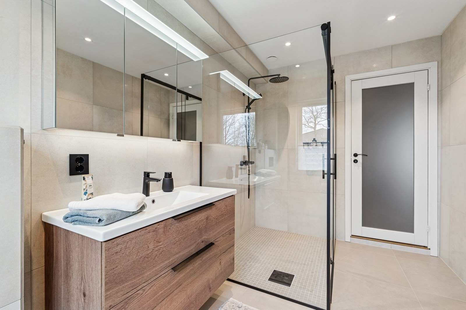 Badet har fine beige fliser på gulv og vegger som står godt til de sorte detaljene. Galleribilde