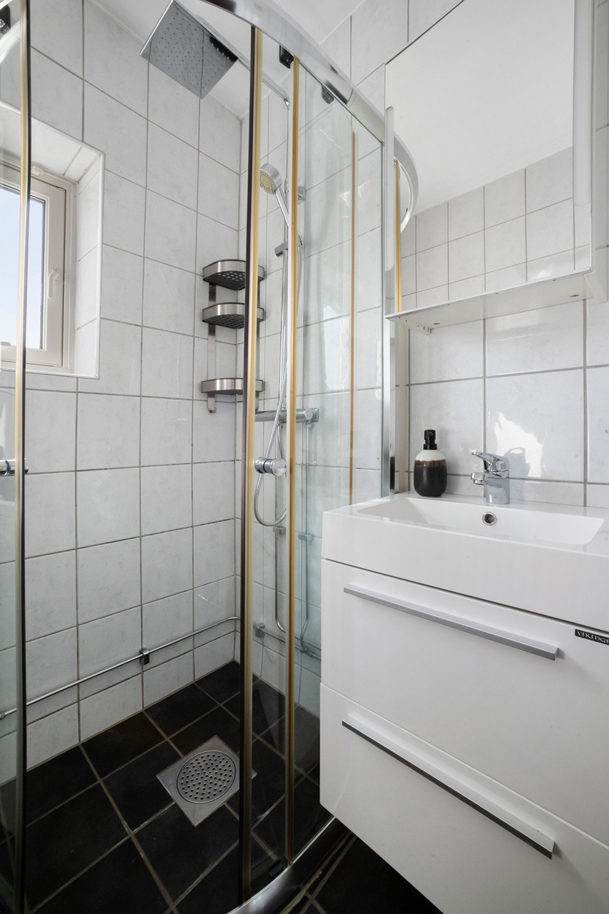 Baderomsinnredningen er bestående av servant med skuffeseksjon, speilskap med sidelys, gulvmontert klosett, dusjhjørne med skyvedører og opplegg for vaskemaskin. Galleribilde