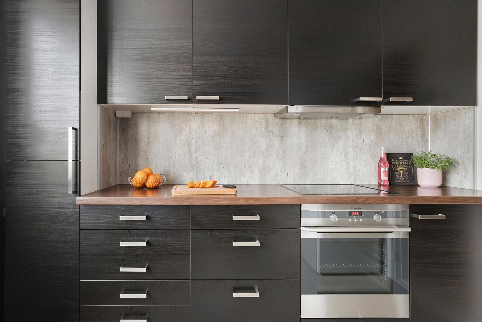 Ikea kjøkkeninnredning med glatte finerte skapfronter, laminert benkeplate med sprutplate på bakvegg, enkel oppvaskkum, ventilator og innfelte hvitevarer som koketopp, stekeovn, oppvaskmaskin, frittstående kjøl/- fryseskap Galleribilde