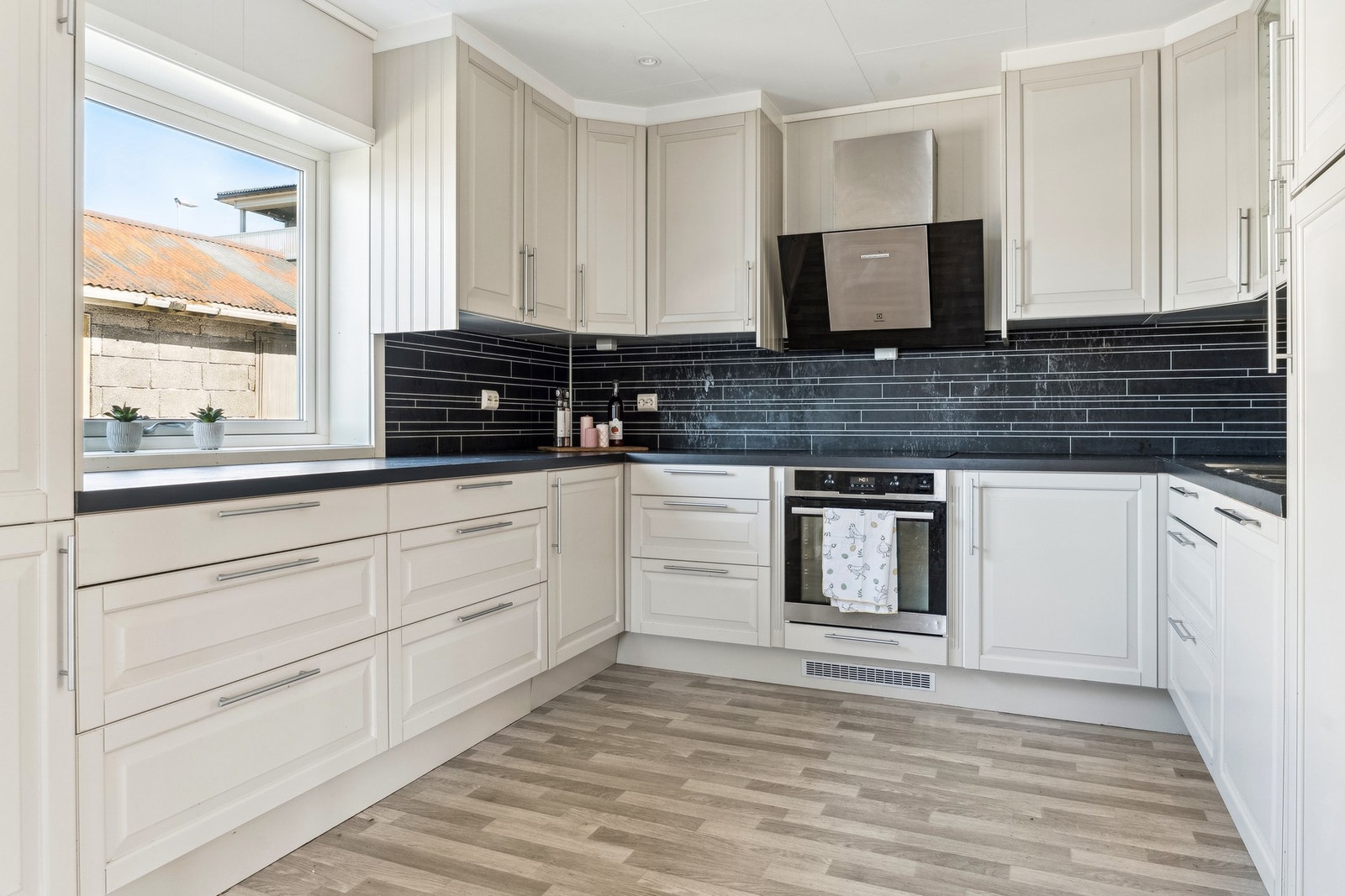 Hvit kjøkkeninnredning med profilerte fronter og benkeplate av laminat. Kjøkken har integrerte hvitevarer og godt med skap og benkeplass. Galleribilde