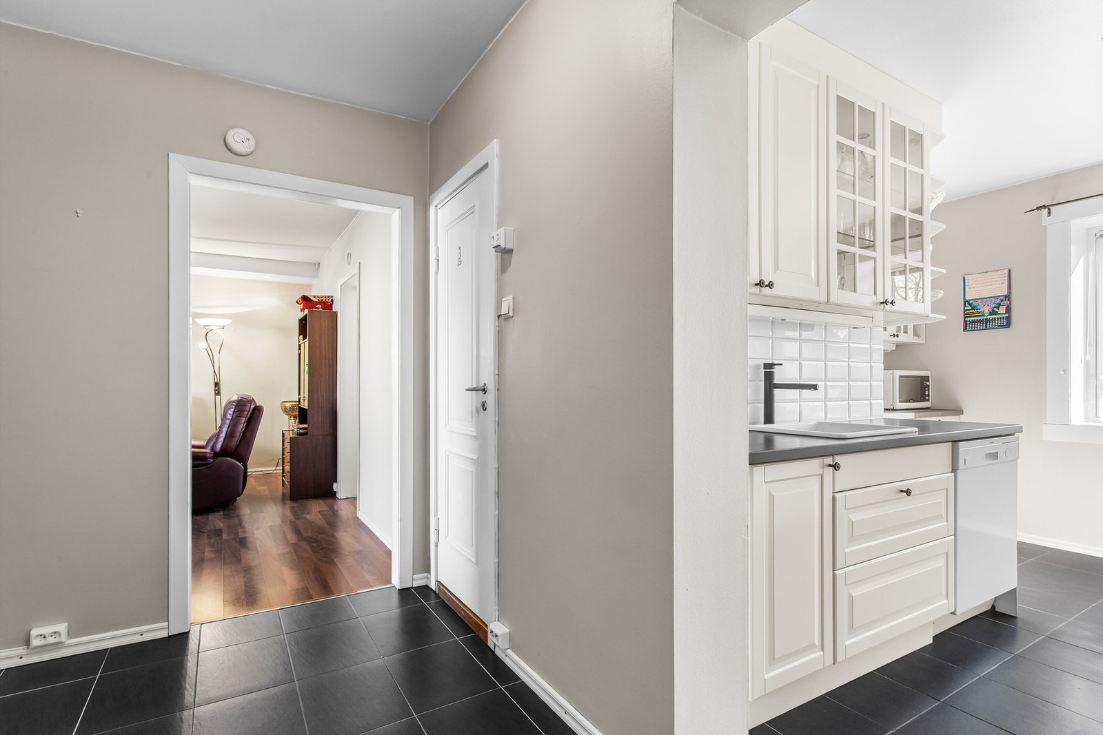 Entré og kjøkken med flislagt gulv og lysmalte veggflater Galleribilde