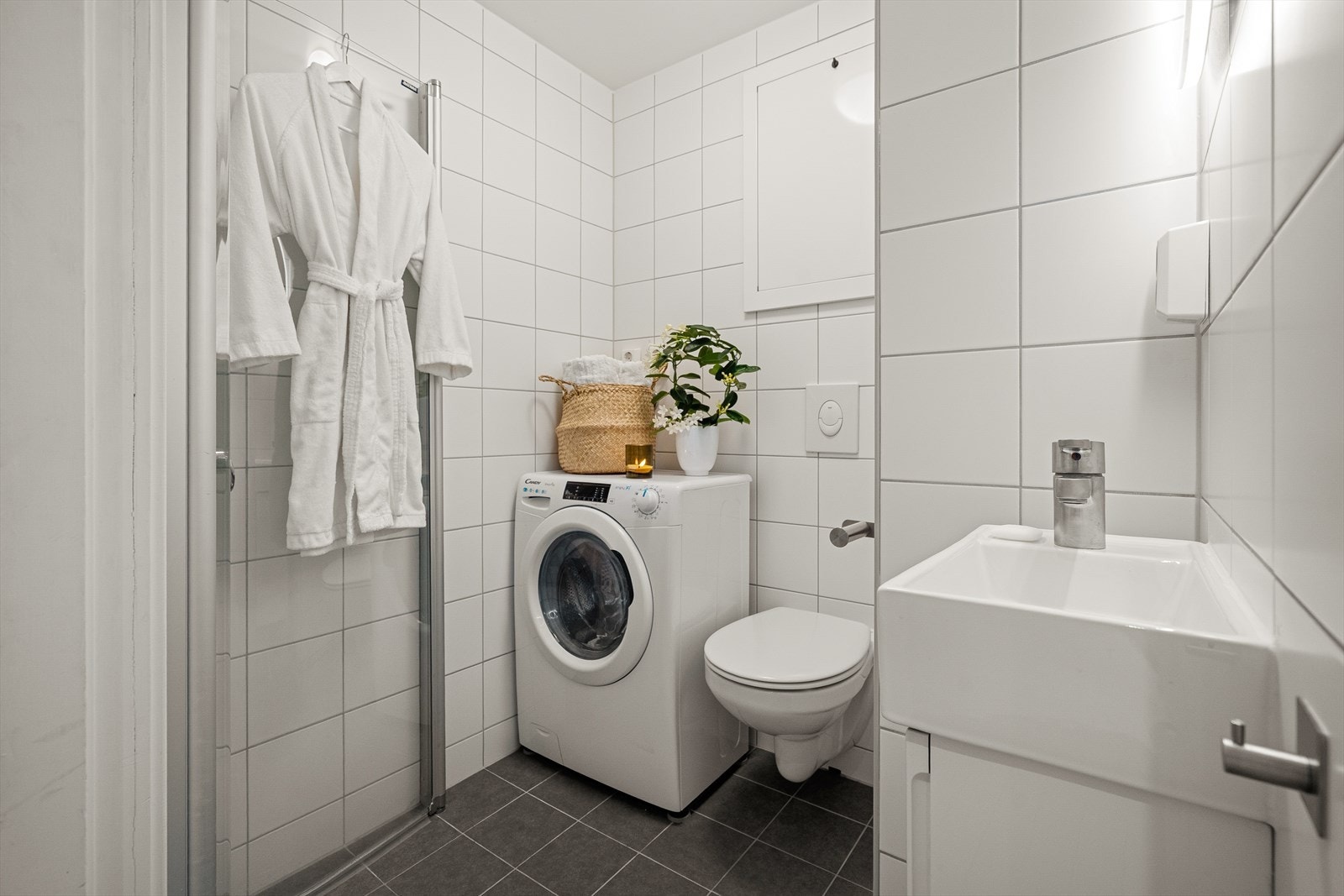 Fliselagt bad fra 2021 med veggmontert WC, dusjplass med vegger, servant med ettgreps blandebatteri i innredning og mulighet for vaskemaskin. Galleribilde