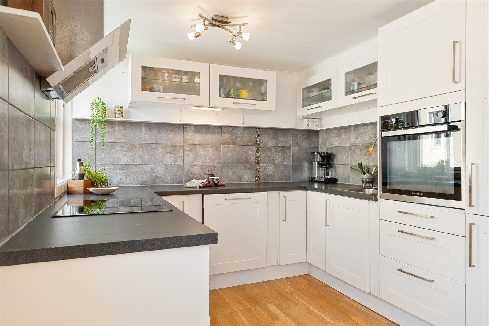 Tidløs innredning med lyse, glatte fronter, fliser på vegg over kjøkkenbenk og benkeplate i laminat. Galleribilde