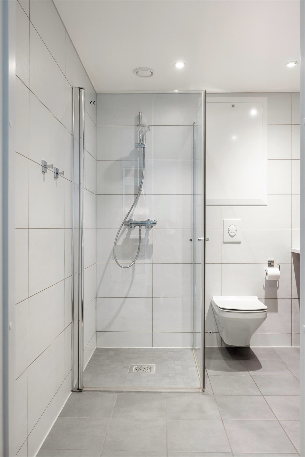 Badet er videre innredet med vegghengt toalett, opplegg for vaskemaskin og nedsenket dusjhjørne med rette svingdører og termostatstyrt blandebatteri. Galleribilde