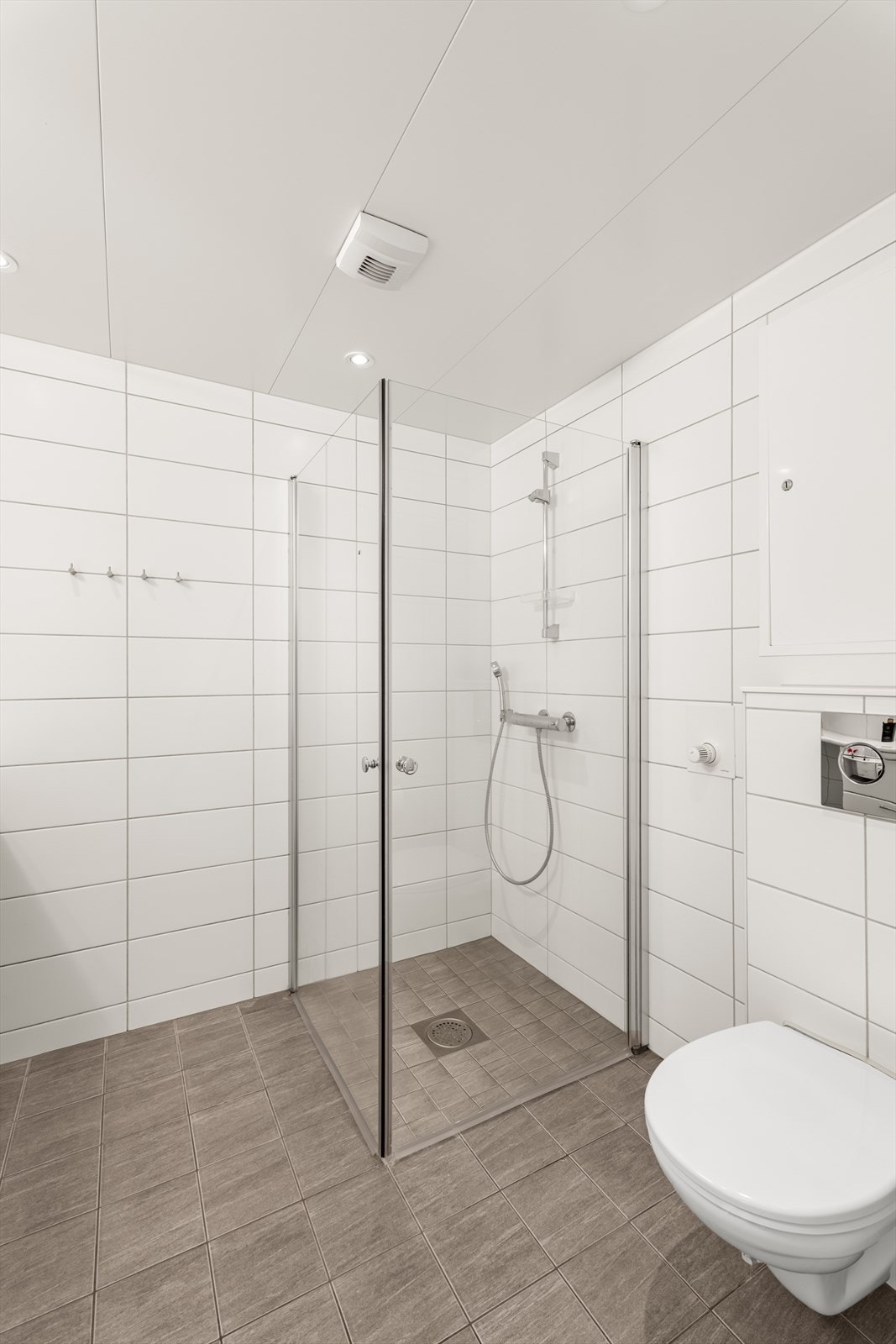 Badet er av god størrelse med opplegg for vaskemaskin og tørketrommel under heldekkende servantinnredning Galleribilde