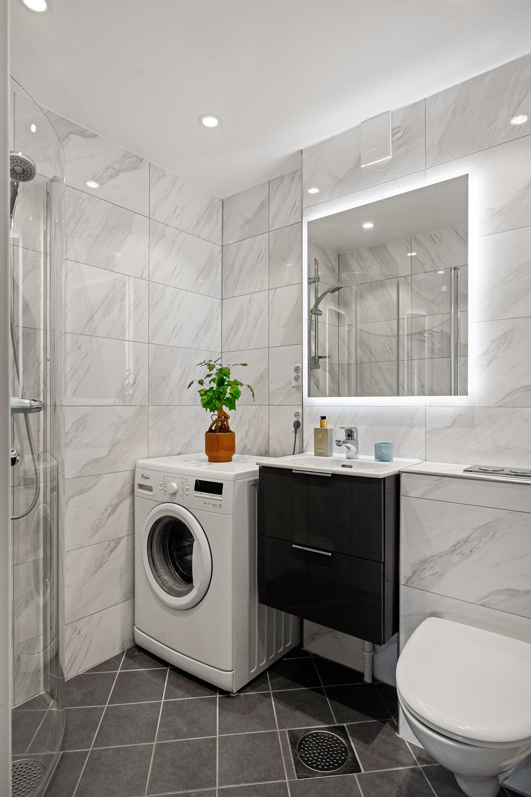 Badet består av servantskap med glatte høyglansfronter og heldekkende servant. Over servanten er det veggmontert speil med lysarmatur. Galleribilde