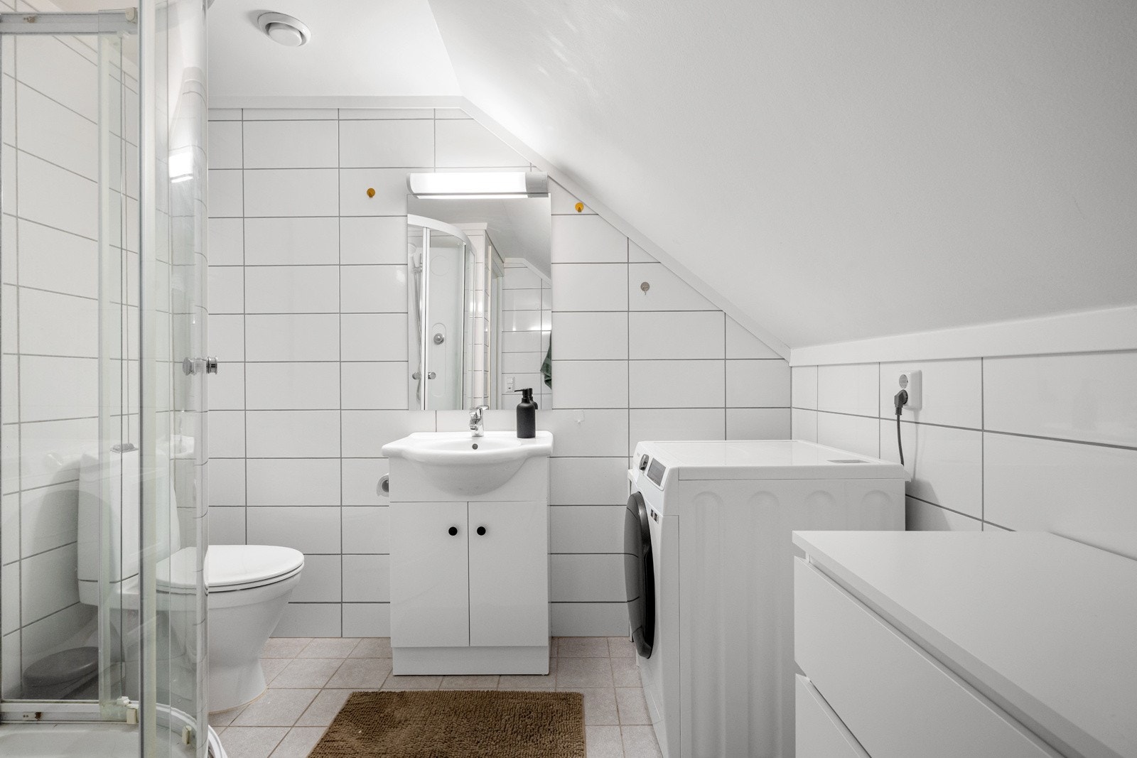 Badet er helfliset med opplegg for vaskemaskin og termostatstyrt varme i gulvet. Badet er innredet med gulvmontert toalett, servant med underskap og dusjkabinett. Galleribilde