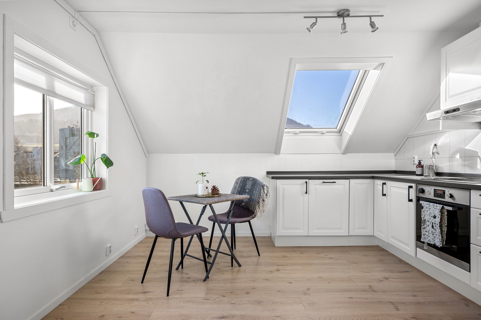 Kjøkkeninnredning med hvite profilerte fronter og mørk benkeplate, integrerte hvitevarer foruten kjøleskap, og med plass til en hyggelig spisegruppe. Galleribilde