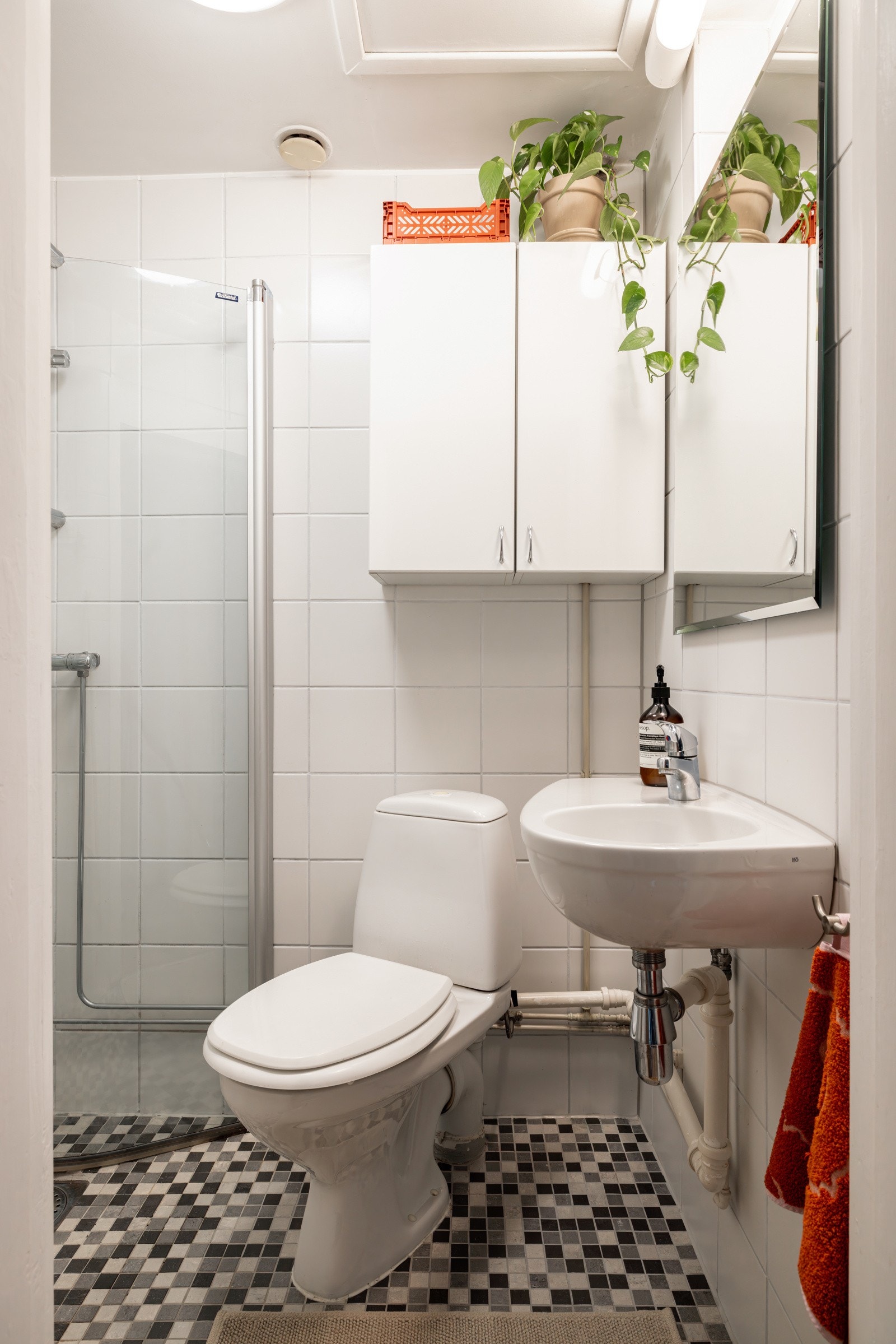 Tidløst baderom med fliser og varmekabler i gulvet. Badet er innredet med toalett, servant, vegghengt skap for oppbevaring og dusjhjørne med innfellbare dusjdører. Galleribilde