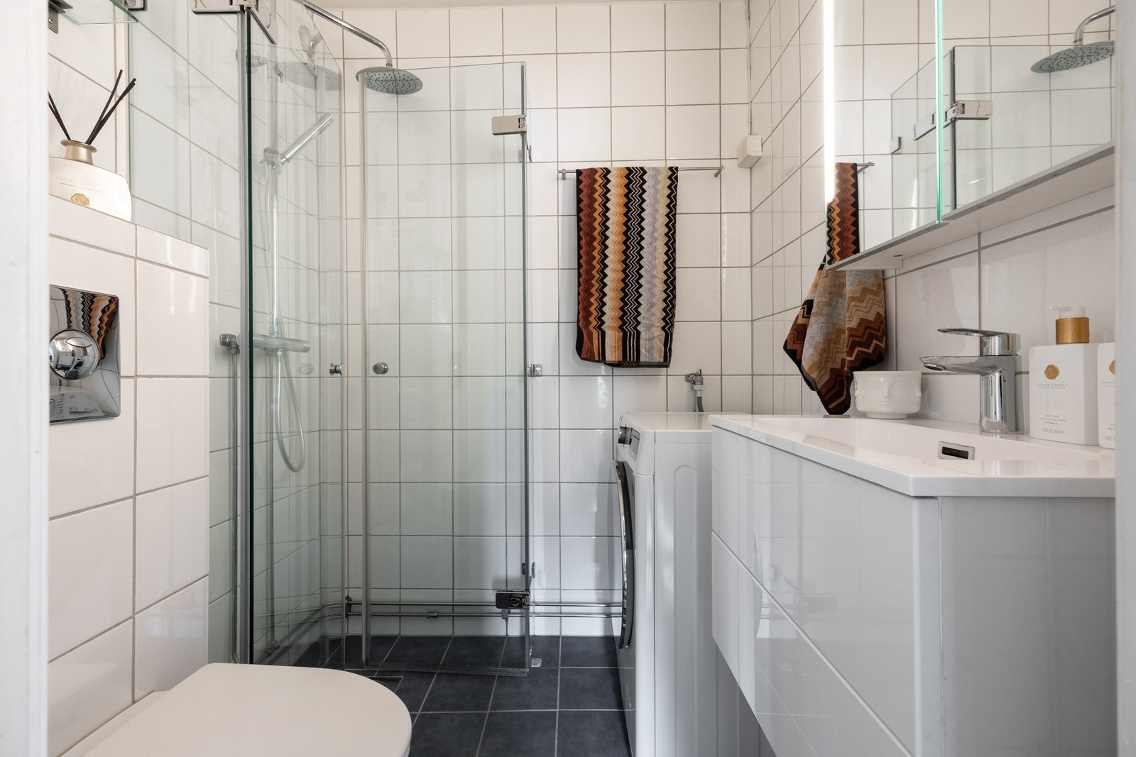 Pent baderom med opplegg for vaskemaskin og mekanisk avtrekksvifte plassert på vegg. Galleribilde