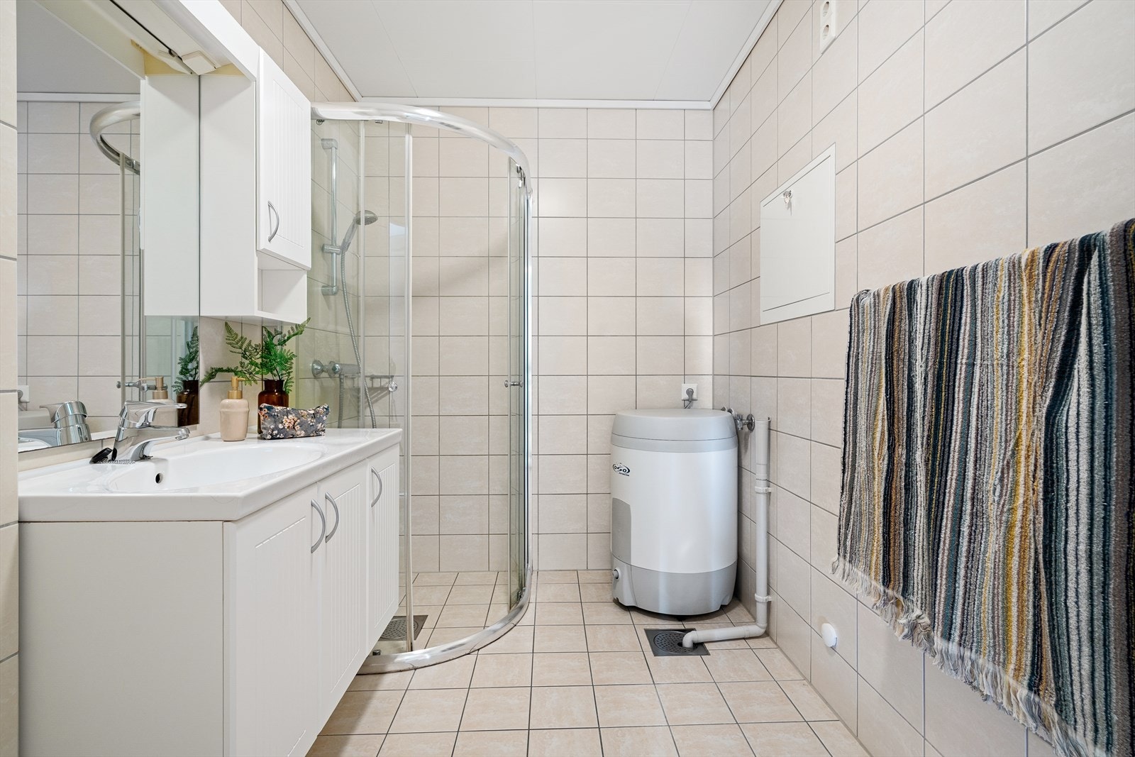 Badet er utstyrt med vegghengt toalett, servant i innredning med speil og overskap, dusjhjørne, opplegg for vaskemaskin og tørketrommel. Galleribilde