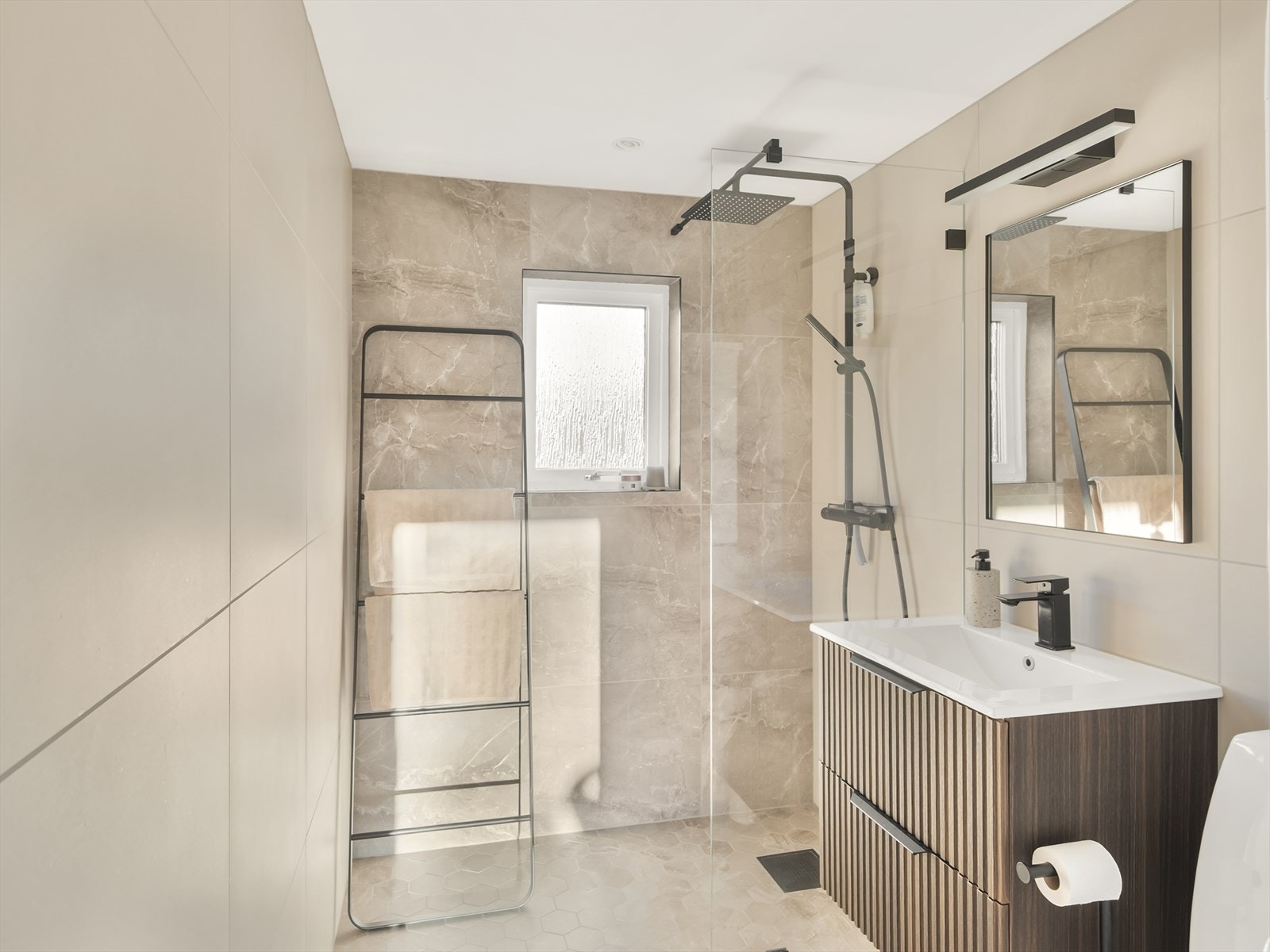 Baderommet er innredet med servant med skuffeseksjon, speil med overlys, gulvmontert klosett, dusjhjørne med regndusj og fast montert glassvegg og opplegg for vaskemaskin. Galleribilde