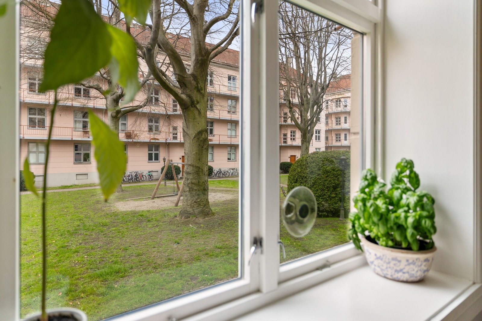 Stue og kjøkken vender ut mot en skjermet og rolig bakgård, som på sommerstid blir til et hyggelig, grønt fellesområde med hagemøbler - perfekt for sosiale sammenkomster og late dager i solen Galleribilde