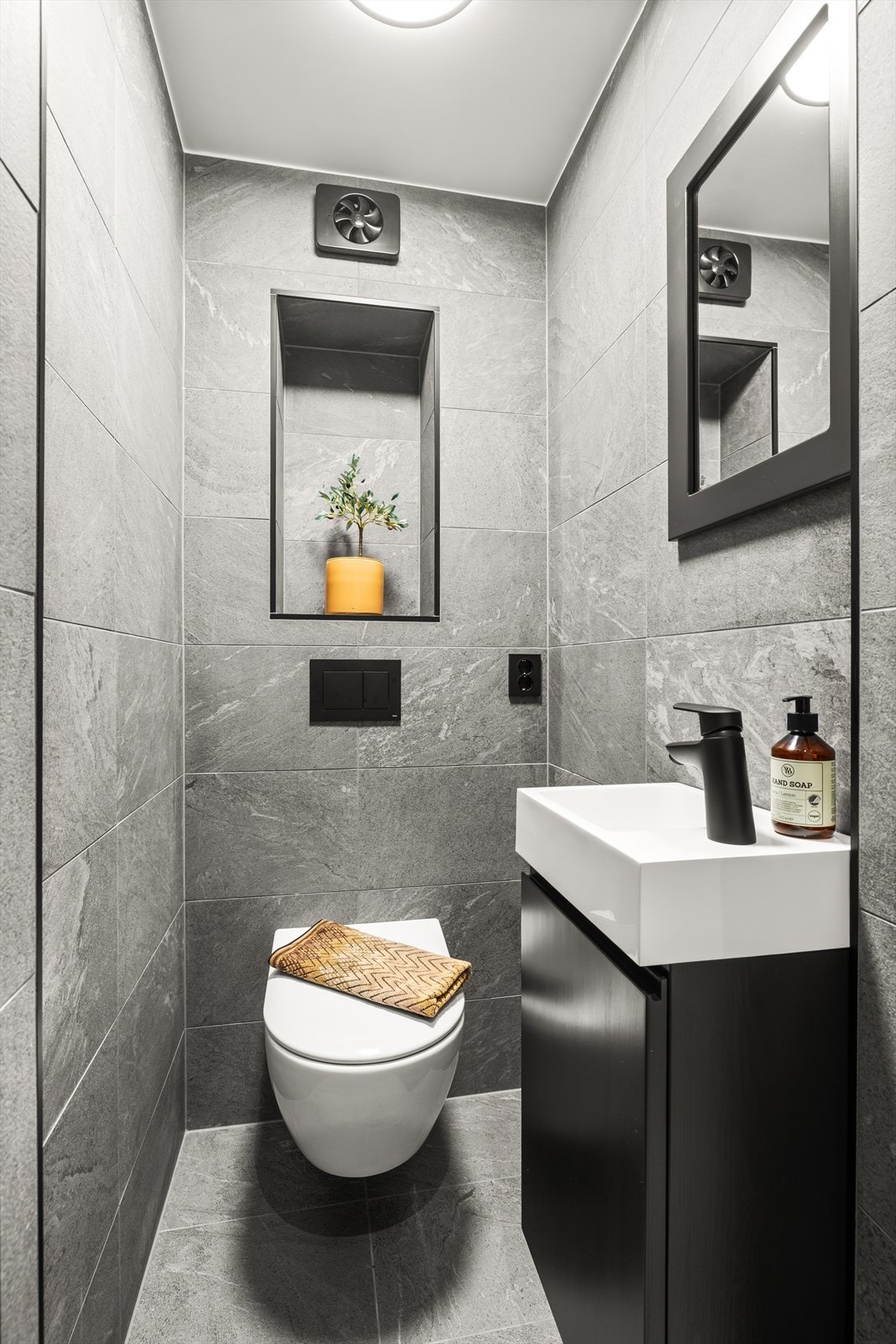 Stilrent toalettrom i 1. etasje med grå fliser, vegghengt toalett, servant med sort innredning og downlights. Galleribilde