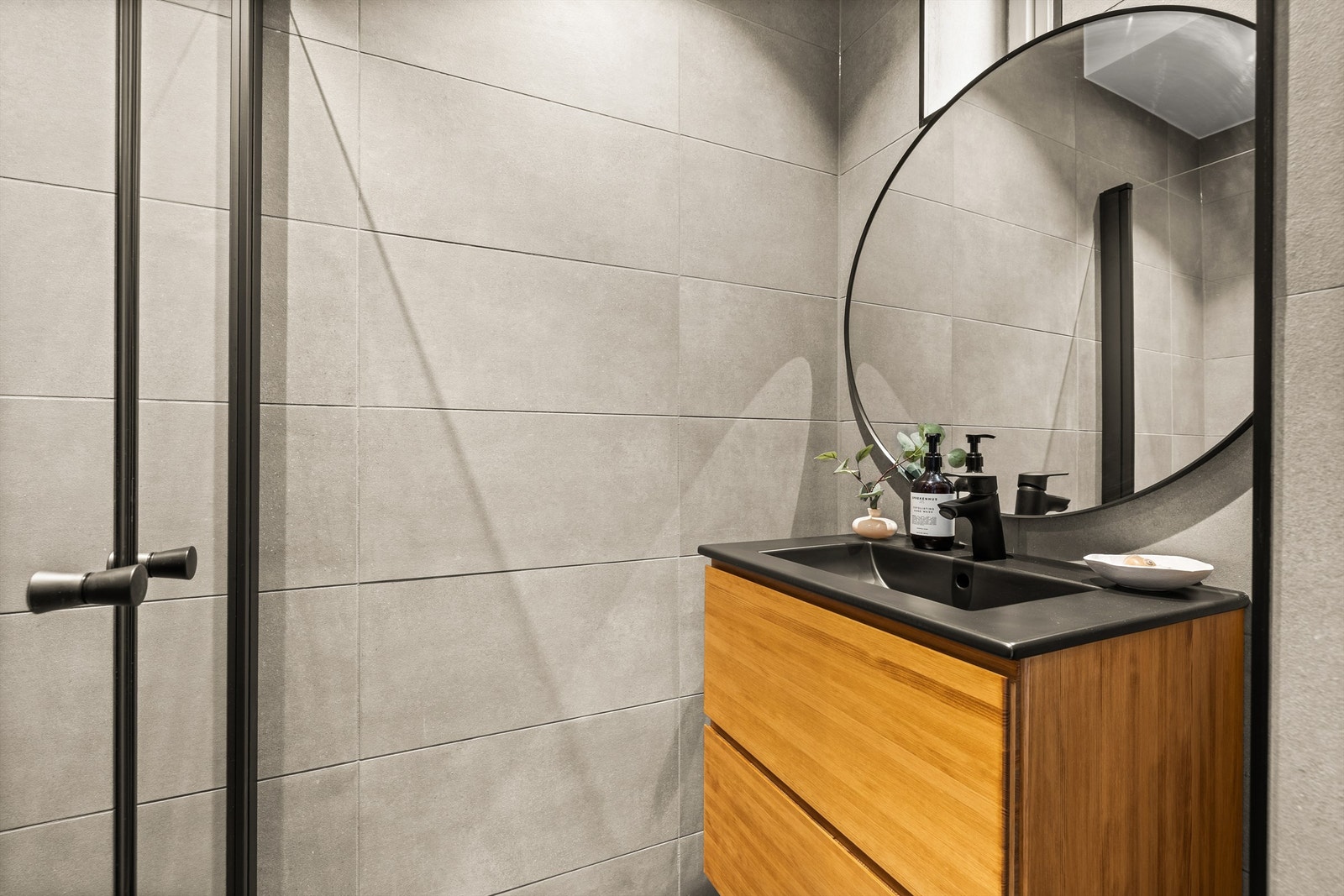 Badet er fra 2025, og er lekkert utformet med gråbeige fliser på gulv og vegger, gulvvarme, downlights og sorte detaljer på alt fra armaturer, lister, trykkplater, stikk og brytere, som gjør det hele ekstra elegant. Galleribilde