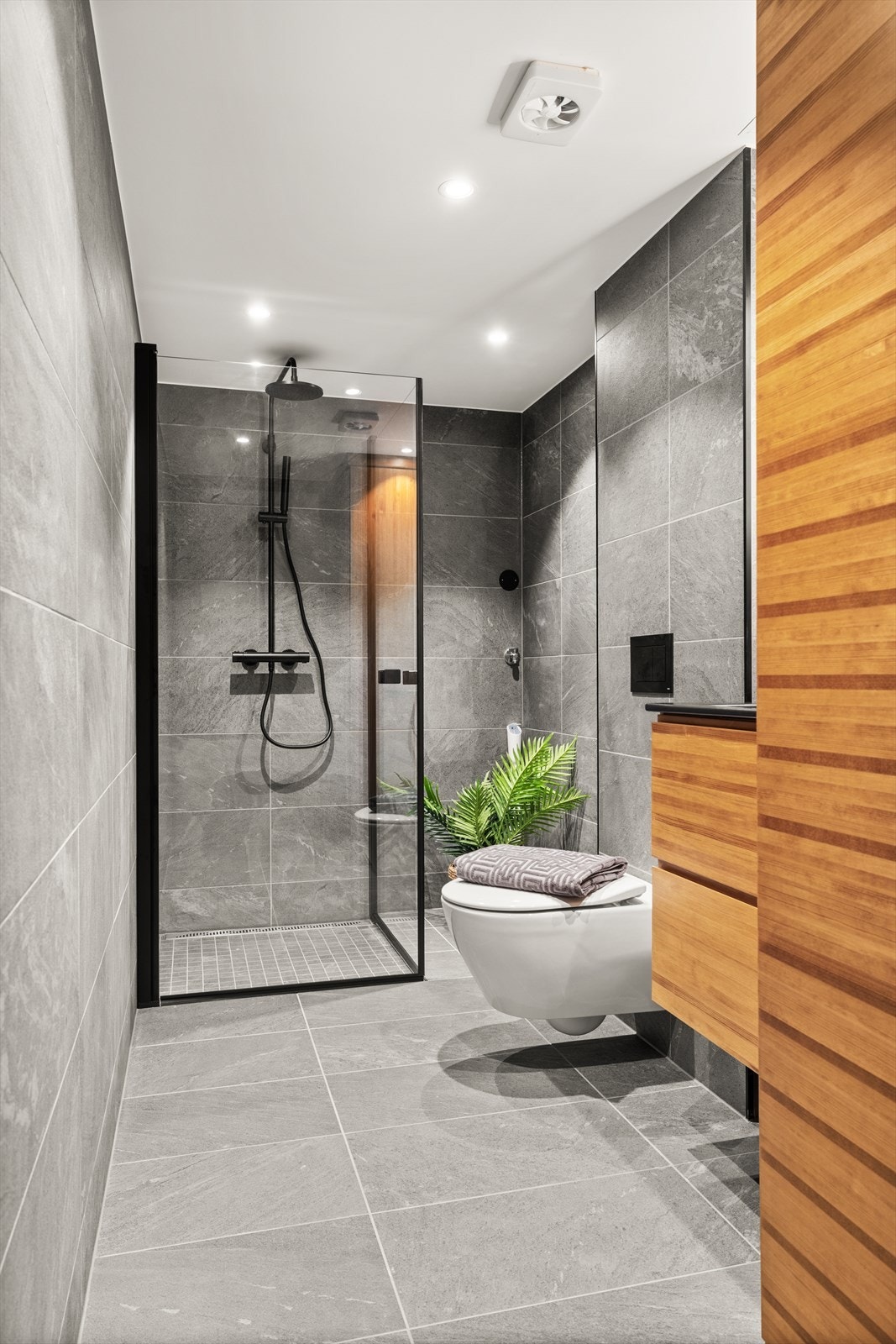 Det er benyttet steinmønstrede, grå fliser på gulv og vegger, downlights i himling og varmekabler i gulvet. Galleribilde