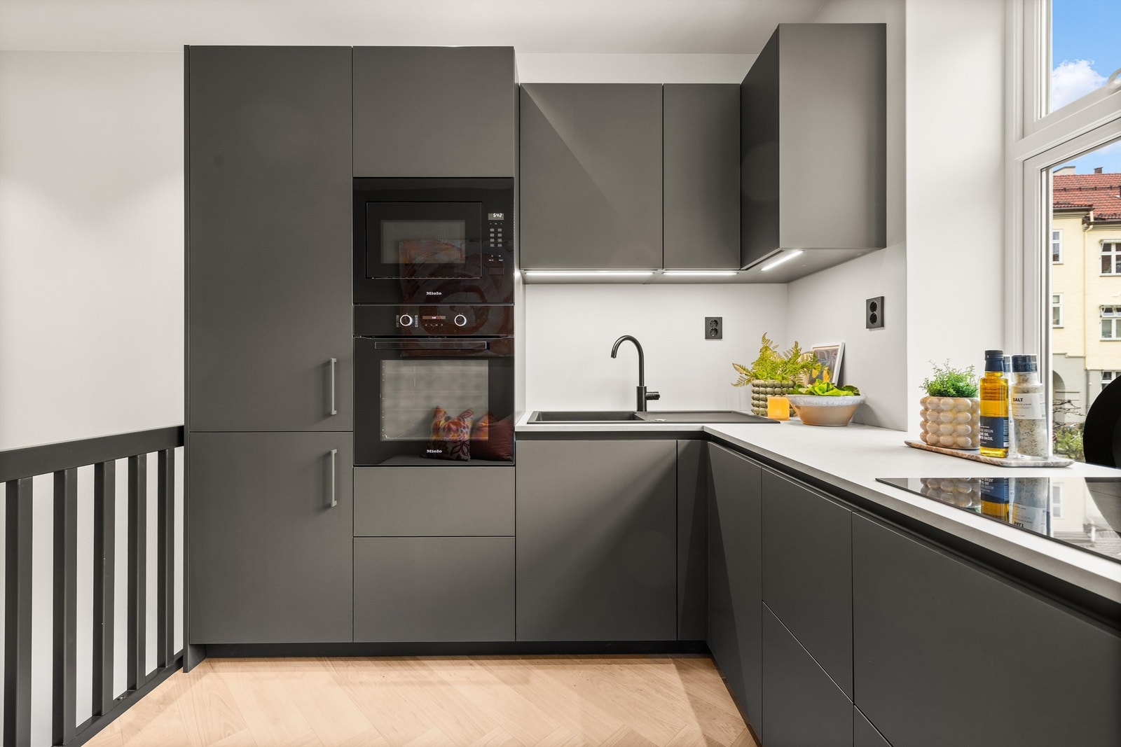 Kjøkkenet har mørke, håndtaksløse fronter i matt finish, benkeplate i lys laminat og vaskekum i mørk kompositt med sort kran. Galleribilde